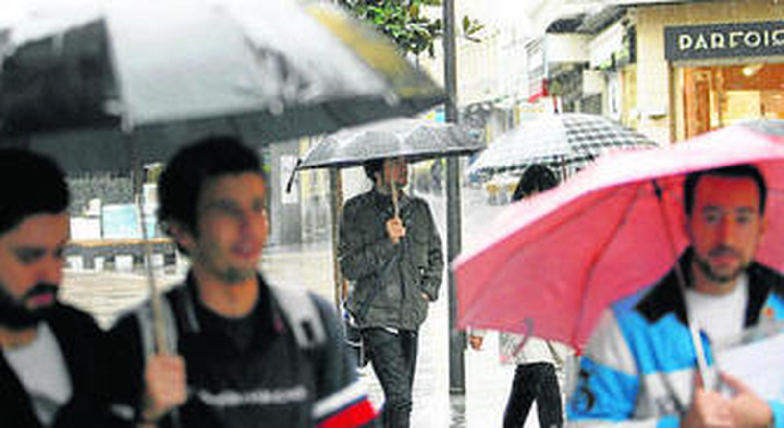 Unos jóvenes caminan por el centro bajo los paraguas.