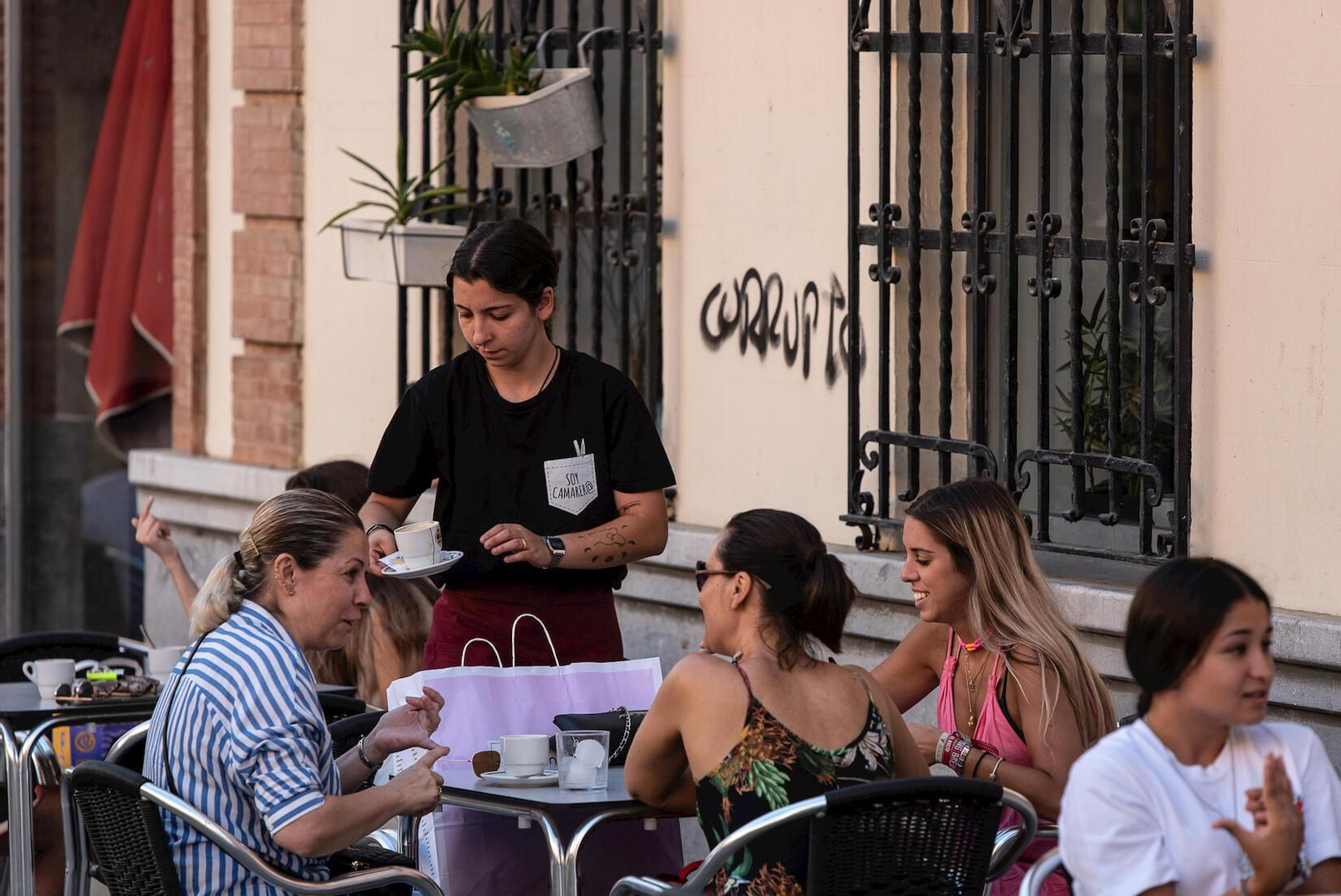 Una camarera atiende a clientes en una terraza.