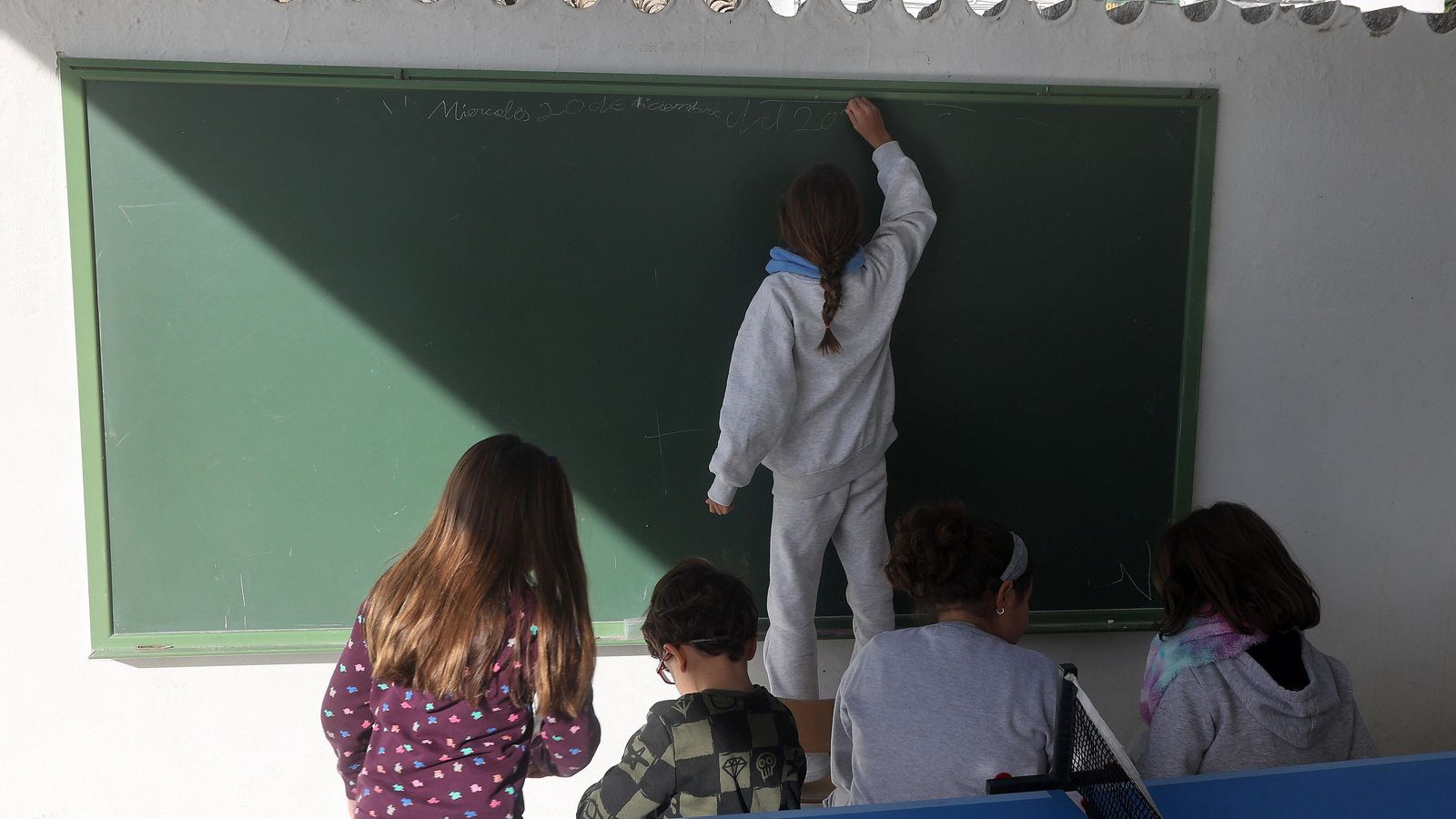 Varios alumnos escriben en una pizarra instalada en el patio del recreo, donde en primavera se imparten clases.