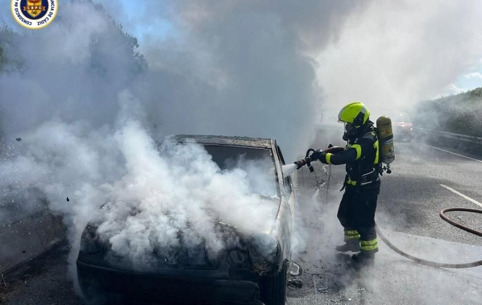 Un bombero del CBPC del parque de Jerez sofocando el vehículo calcinado en la A-4