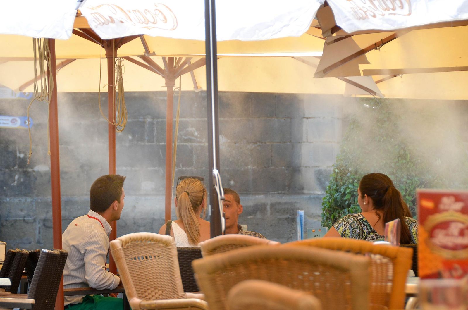Varias personas en un velador bajo una sombrilla con aspersión de agua.