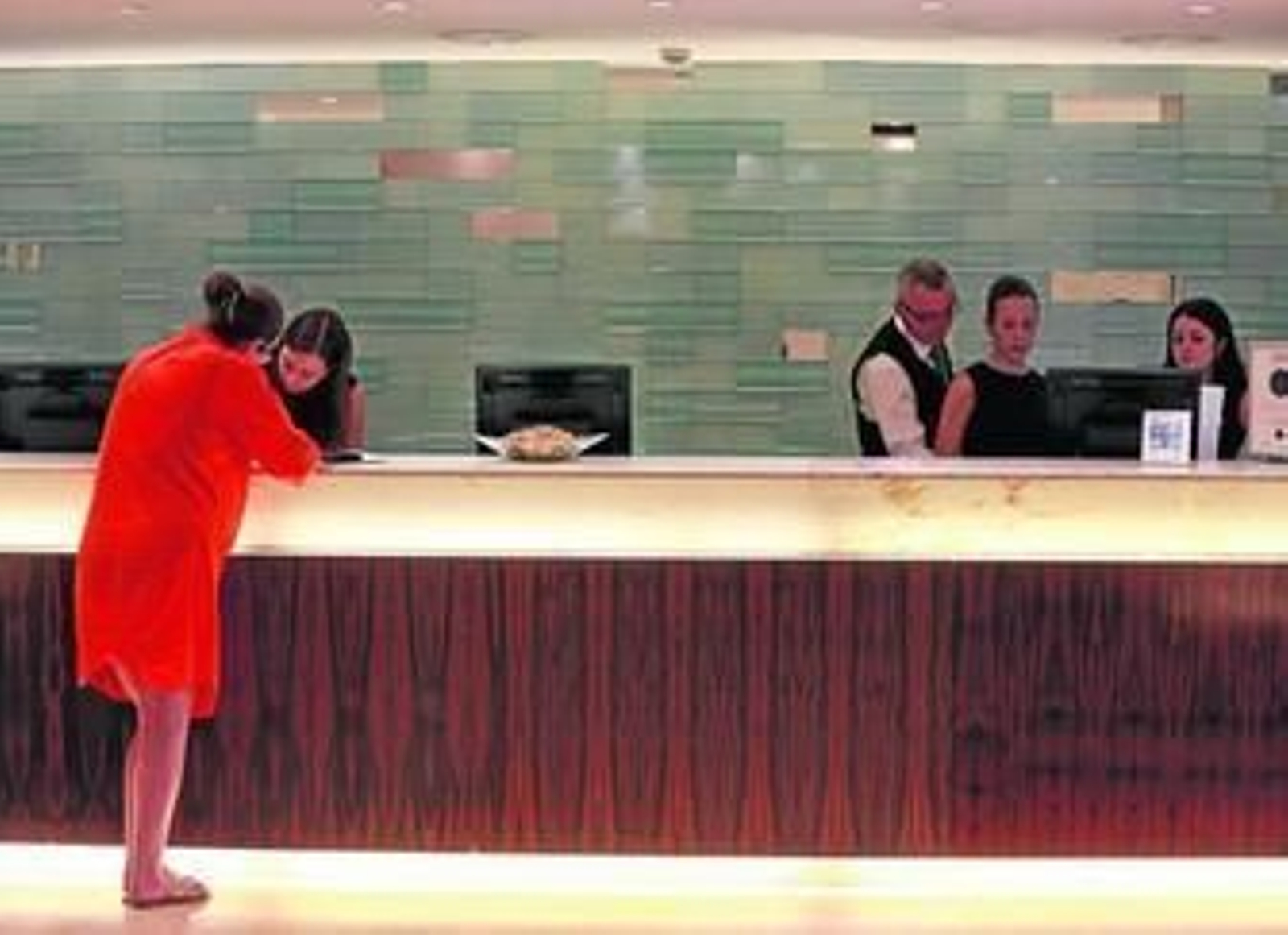 Una recepcionista atiende la petición de una clienta de un hotel.