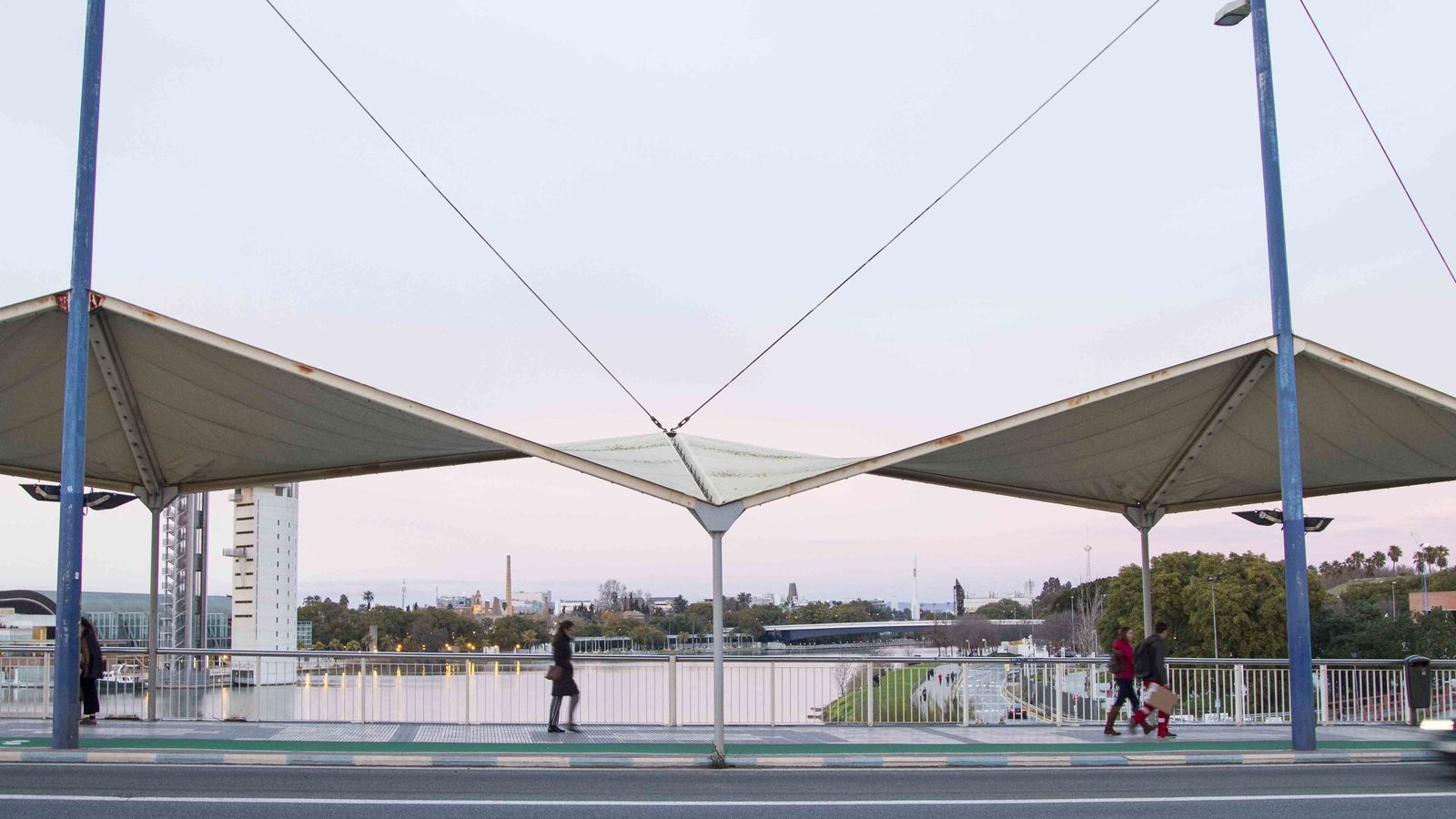 Varias personas pasan por debajo de las deterioradas lonas del puente.