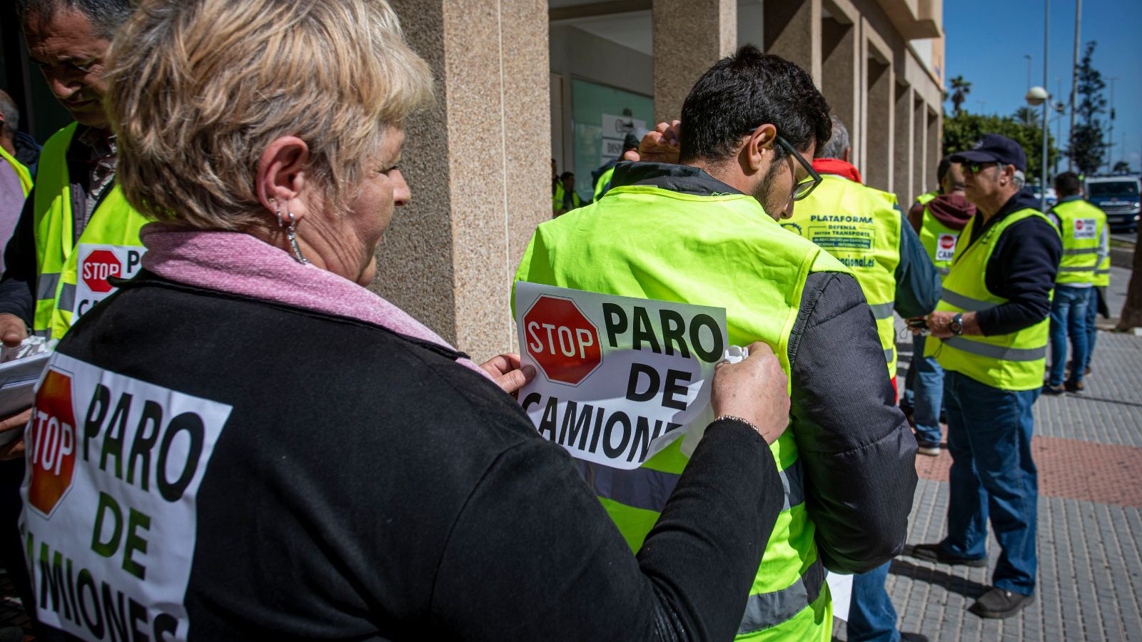Una mujer coloca un  cartel en la espalda de unos de los manifestantes.