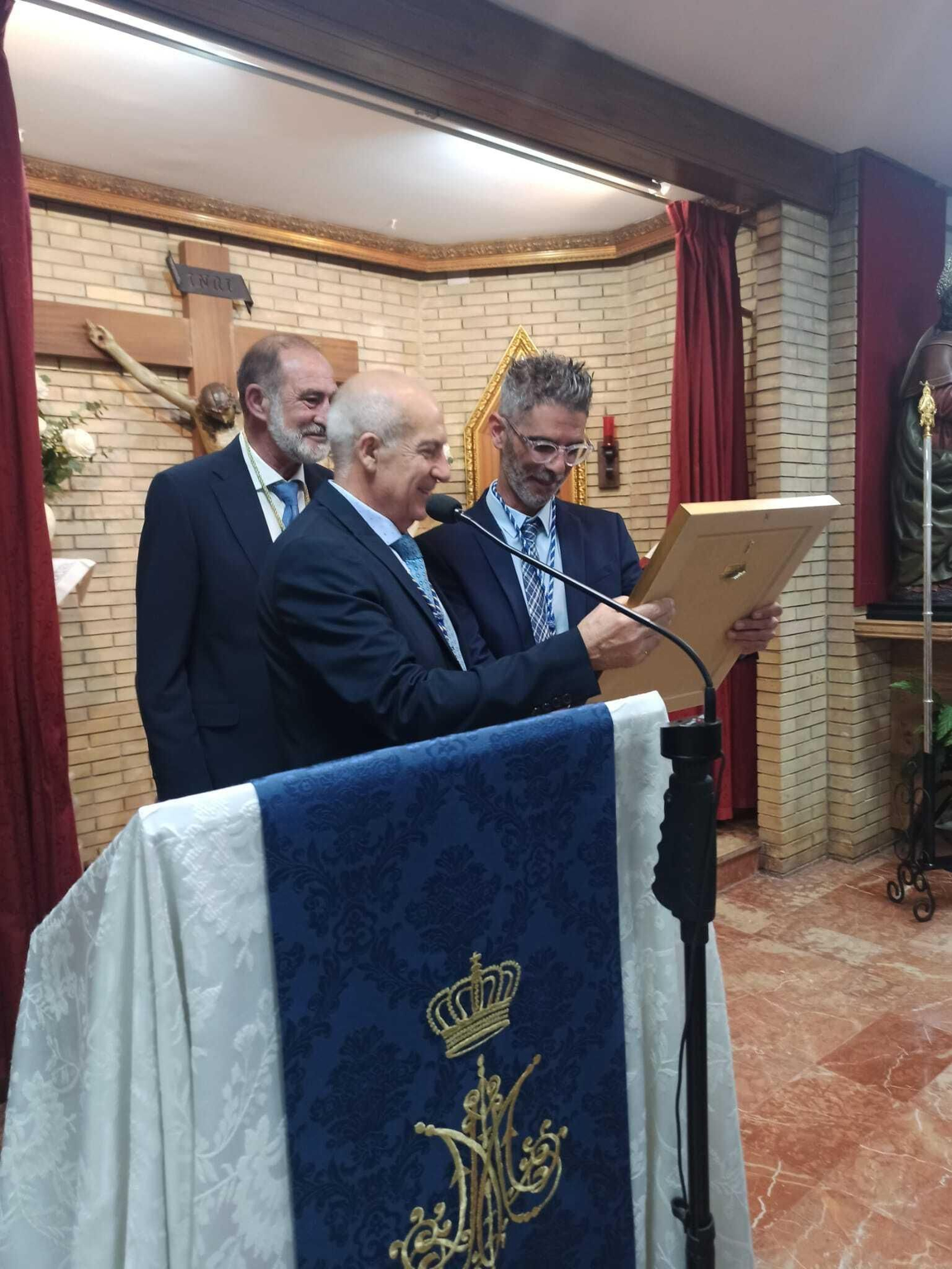 El periodista Rafael Adamuz recibe un obsequio de parte del presidente de la cofradía, Juan Pinto y en presencia del Hermano Mayor de este 2024