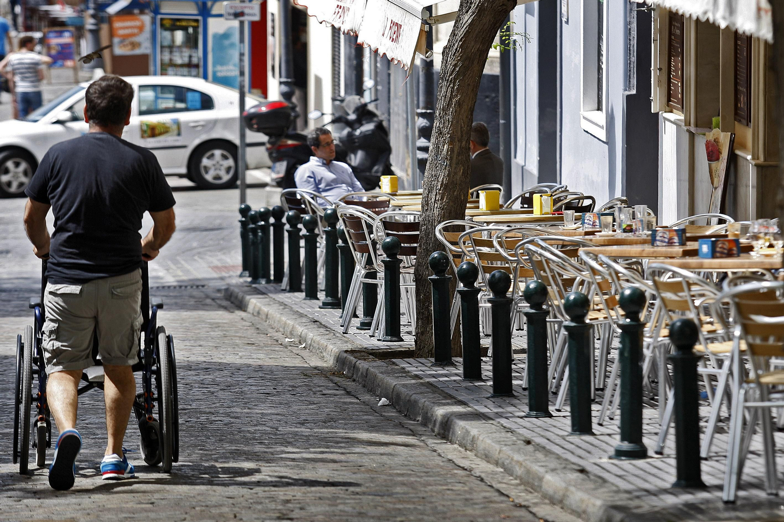 Un hombre transita empujando una silla de ruedas por enmedio de la calzada de la calle Libertad.