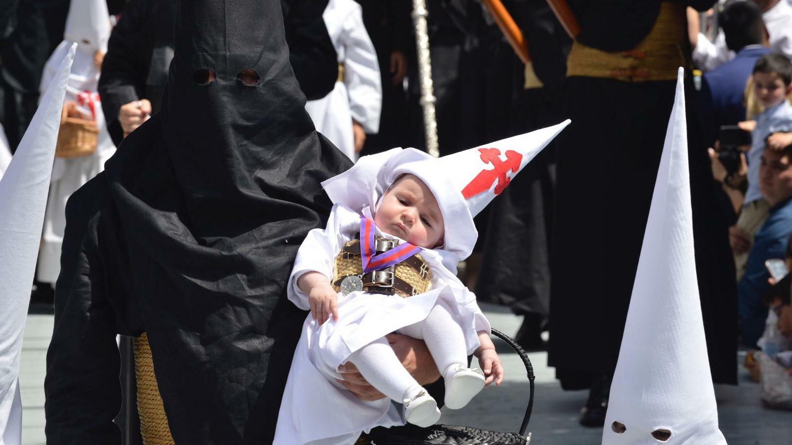 Un nazareno del Amor sostiene en brazos a uno de la Borriquita.