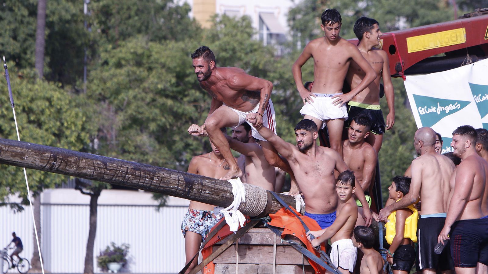Los jóvenes se reúnen en la prueba de la cucaña de la Velá de Santa Ana.