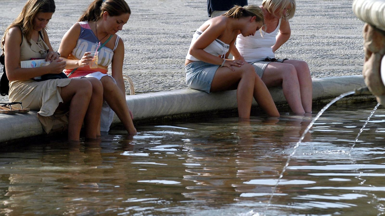 Turistas se refrescan este verano con el agua de la emblemática fuente de la Plaza de España.