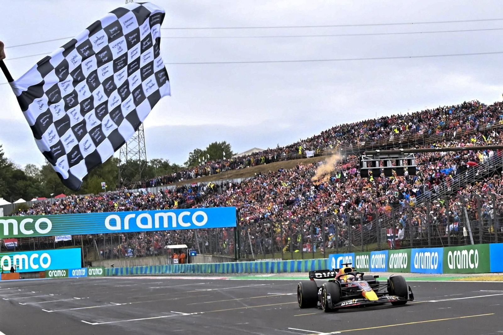 Verstappen cruza la línea de meta en primer lugar con la bandera a cuadros ondeando.