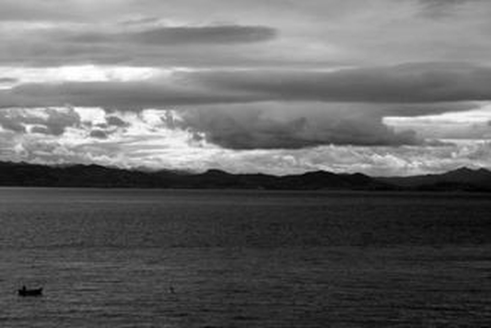 Una pequeña embarcación de pesca navega por las aguas del Estrecho de Gibraltar con el continente africano como fondo.