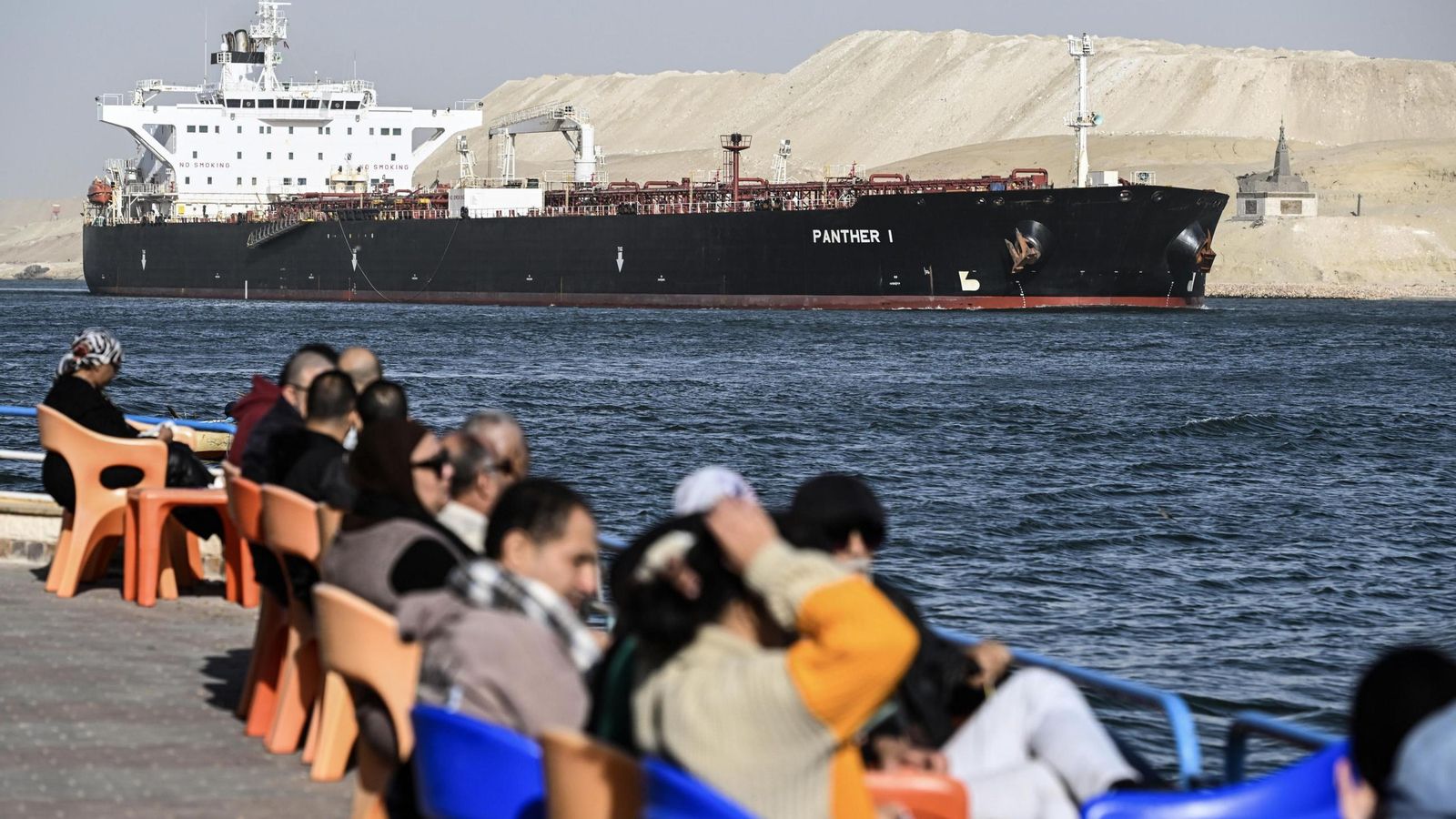 Varias personas observan como un barco cruzan el Canal de Suez hacia el mar Rojo.