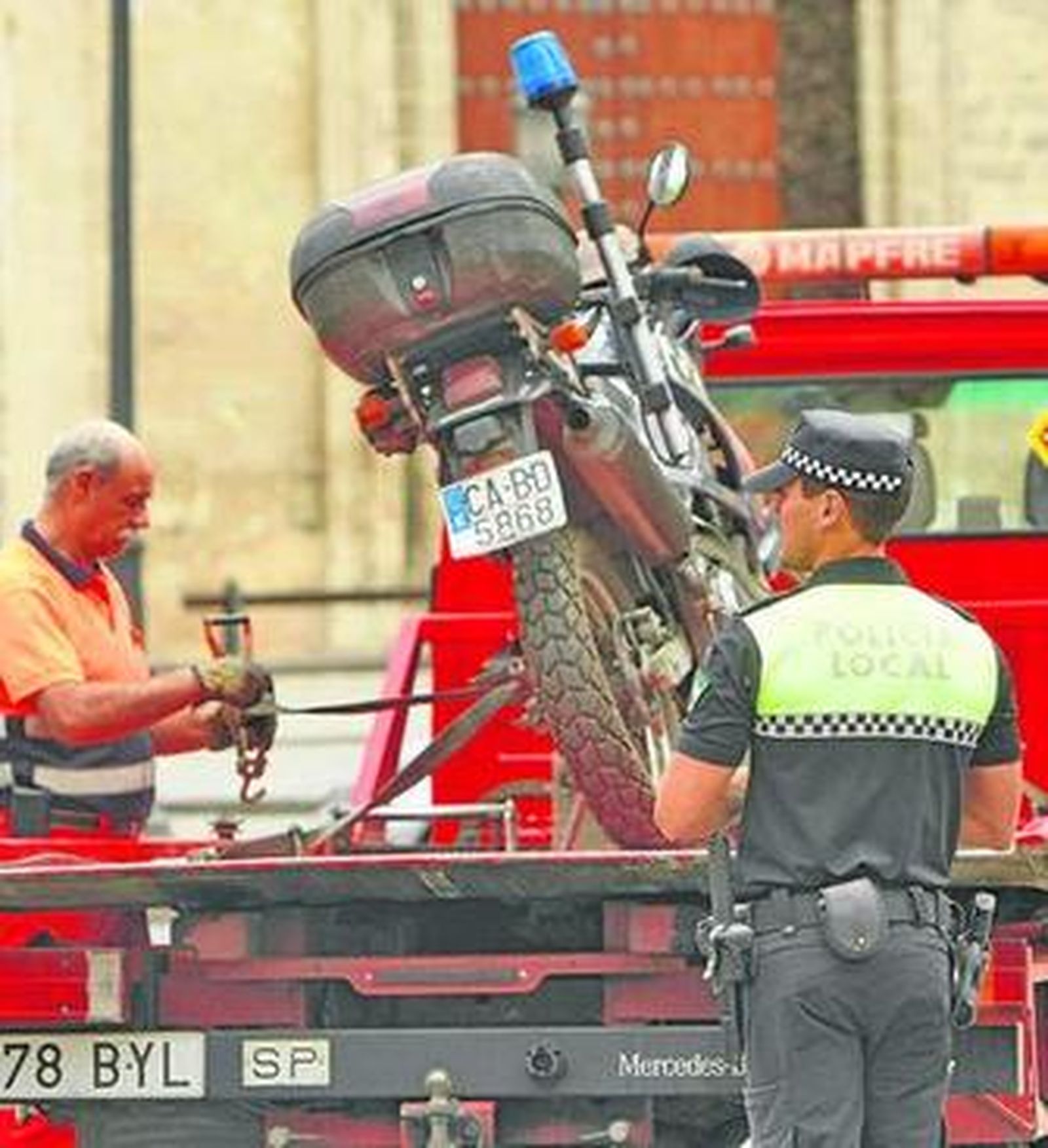 Un agente escolta a la grúa, ayer, con una moto de la Policía Local.