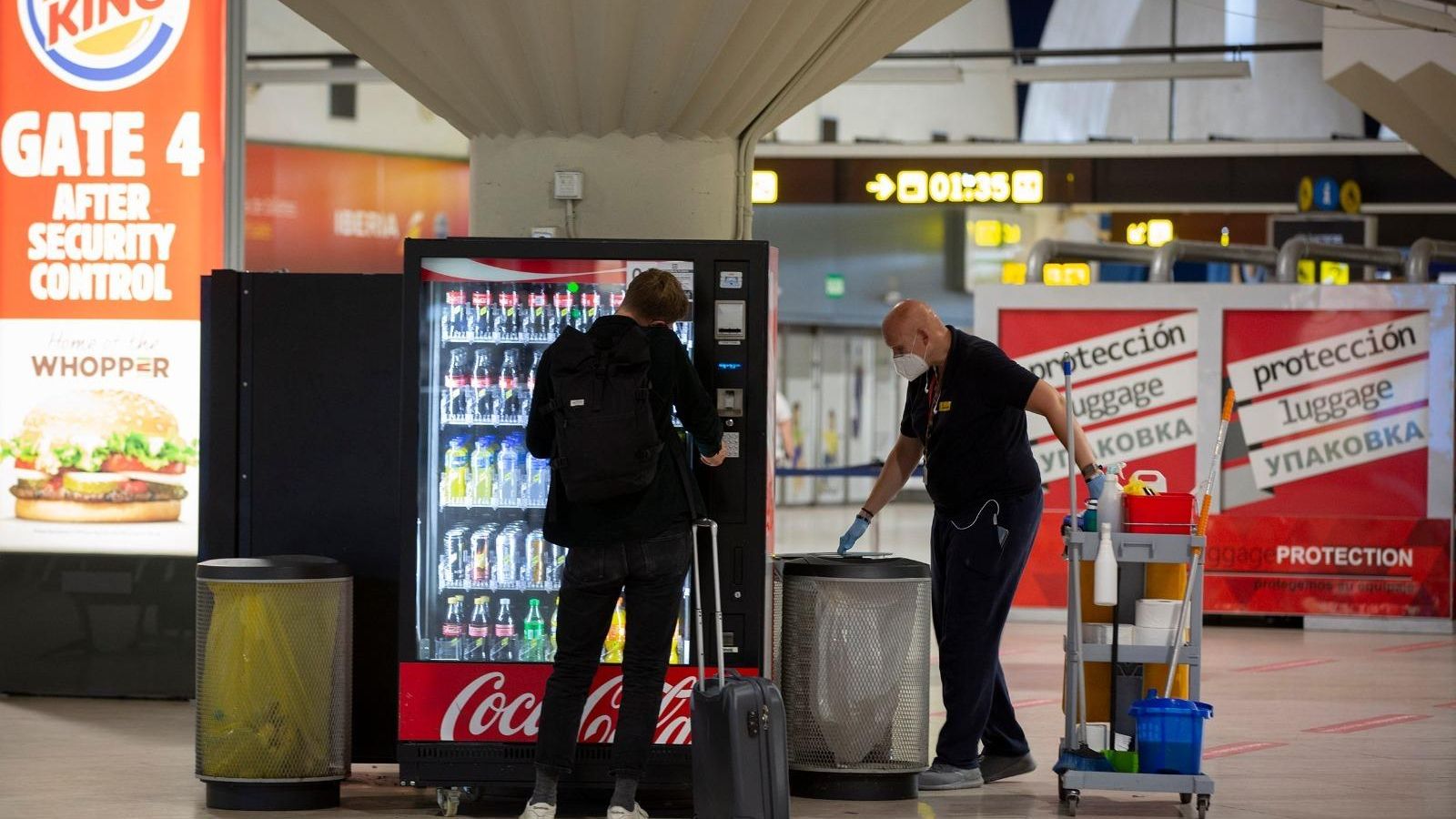 Uno de los pasajeros del vuelo de Londres compra bebidas en una máquina junto a un operario de limpieza.