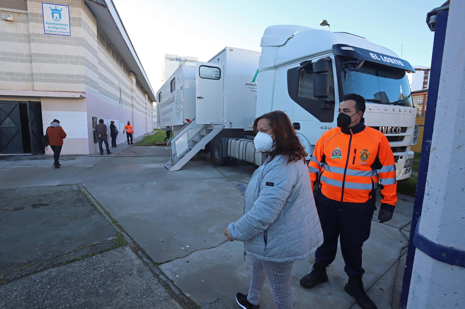 Una mujer y un voluntario de protección civil, junto a la unidad móvil de Salud instalada para el cribado en Algeciras