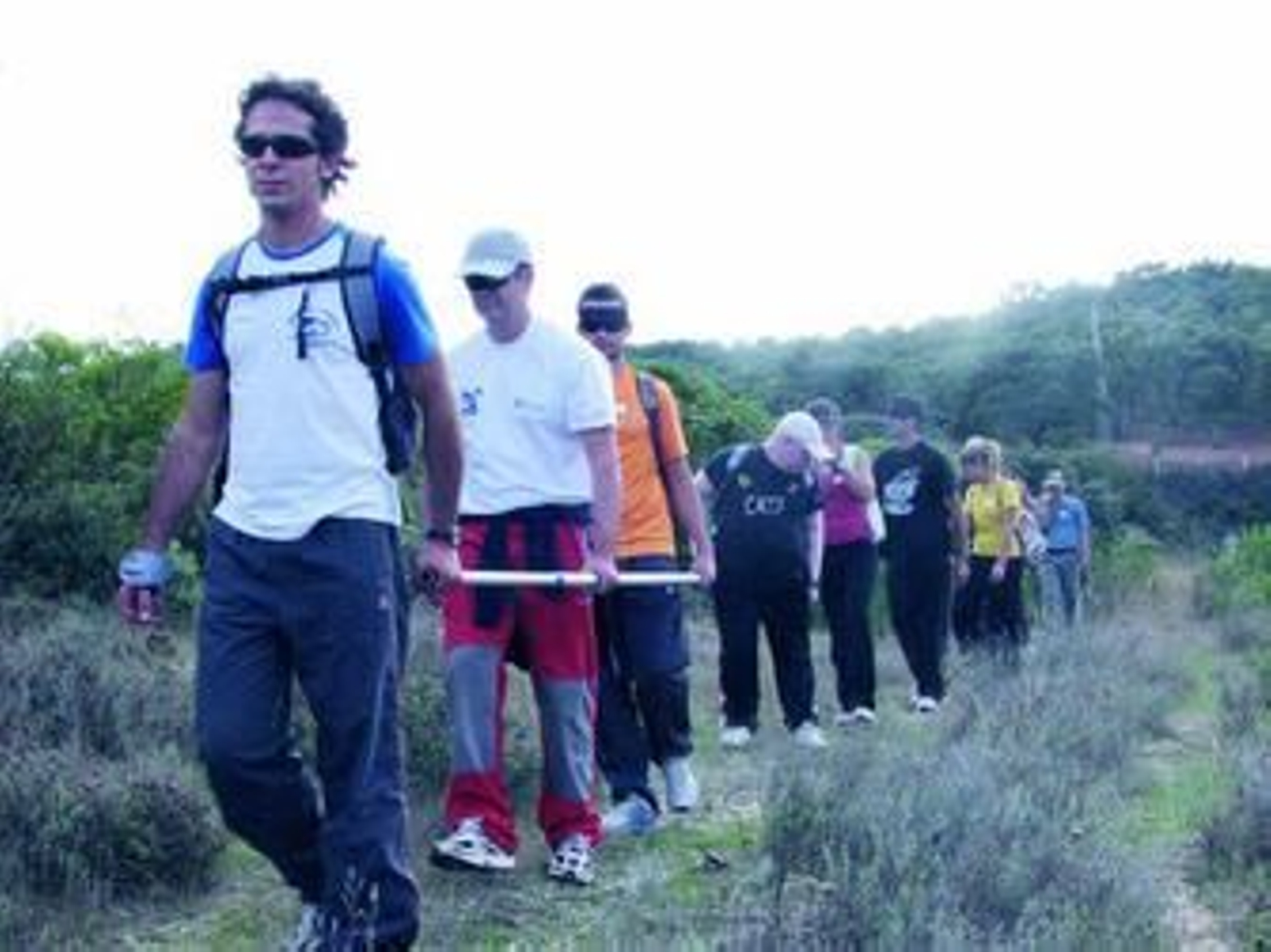 Un monitor marcha en cabeza de un grupo con personas ciegas y otras con antifaces para conocer los problemas a los que se enfrenta quien no ve.