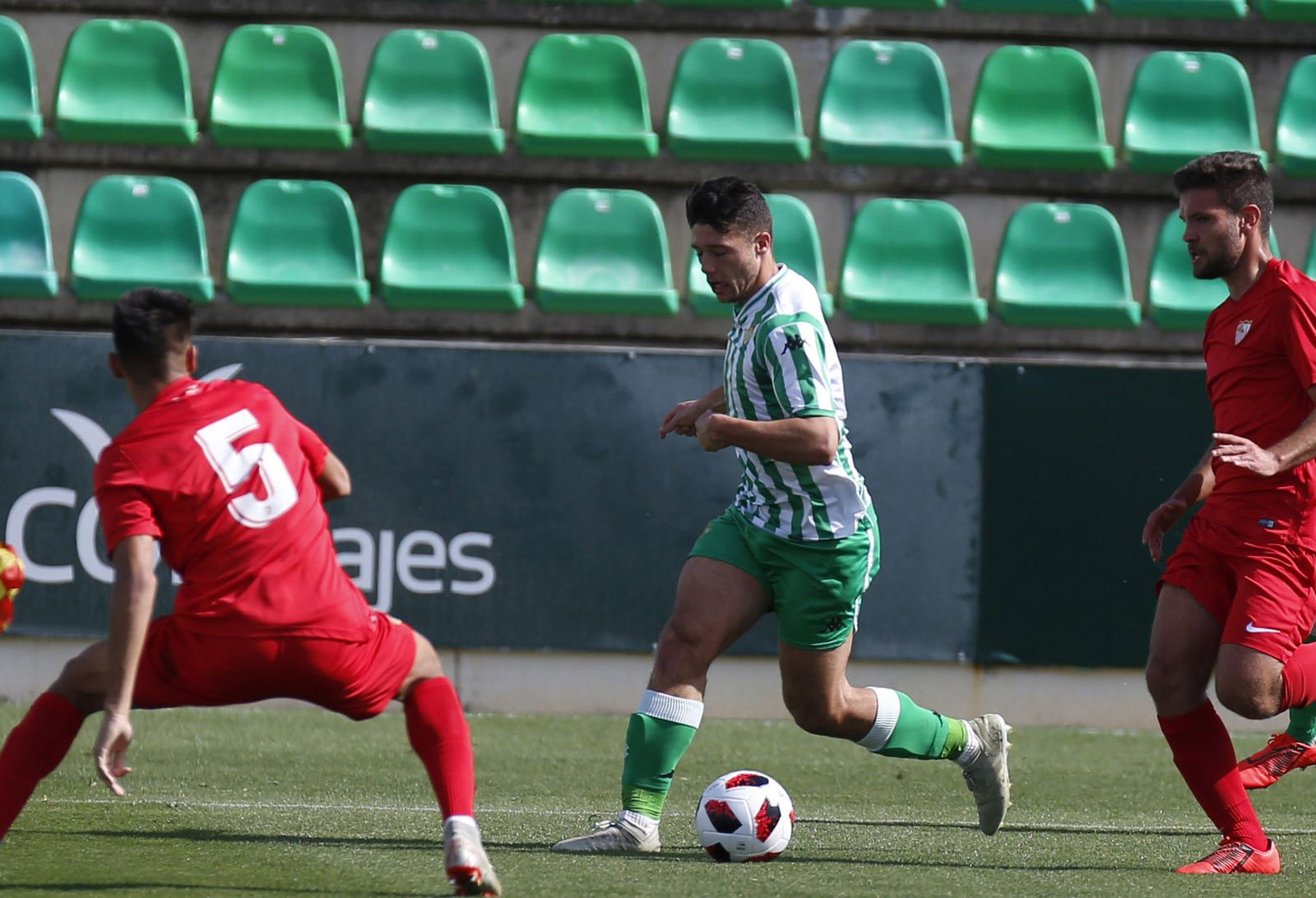 Un jugador verdiblanco trata de zafarse de sus rivales sevillistas en la banda.