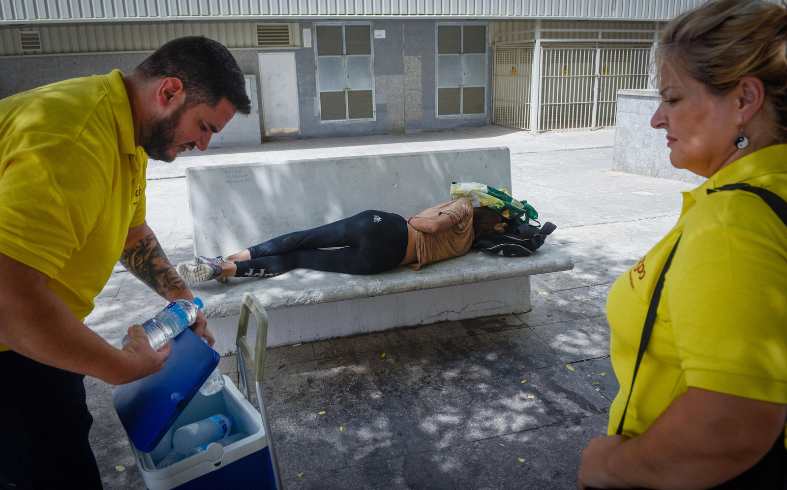 Dos trabajadores de la UMIES ofrecen agua a una mujer, que duerme en un banco en la calle.