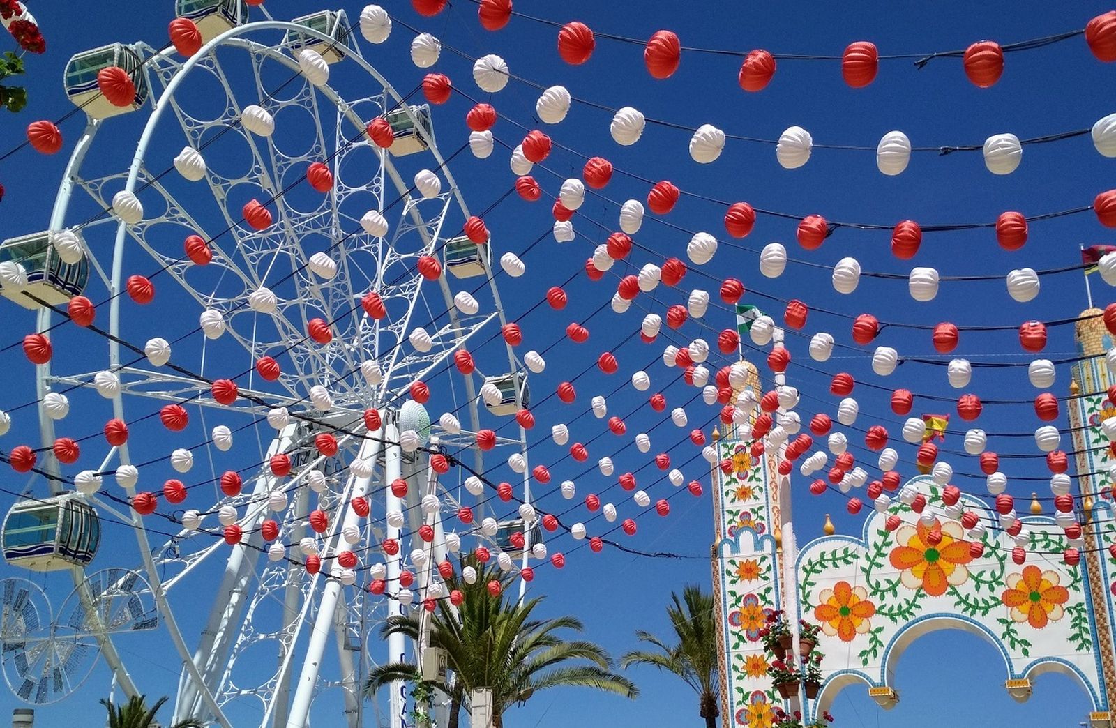 La típica cubierta de farolillos de la Feria de Sanlúcar, junto a la portada y la novedosa noria de esta edición.