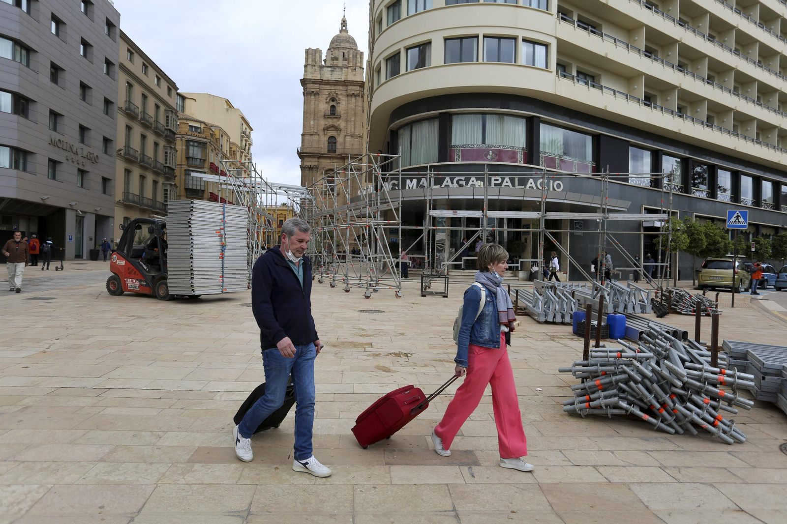 Unos turistas  pasan por delante del montaje de las tribunas para la Semana  Santa  en el centro de Málaga.