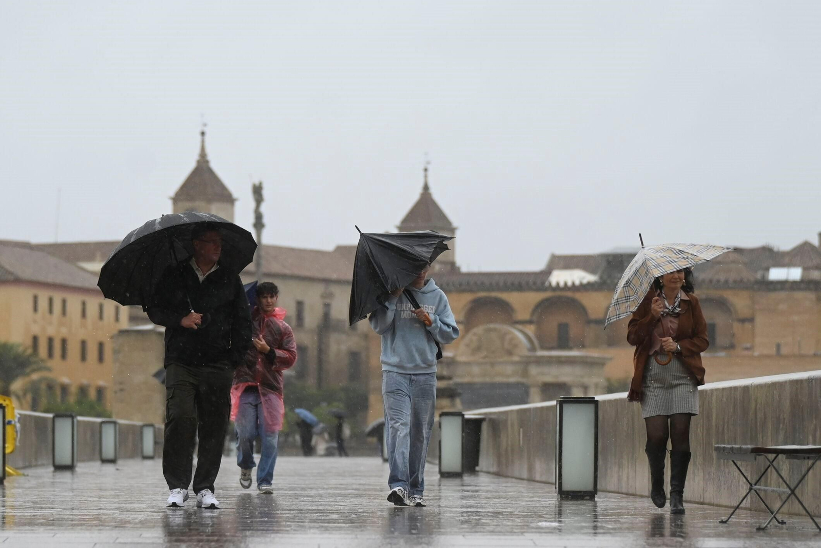 Varias personas luchan contra el viento con sus paraguas abiertos.