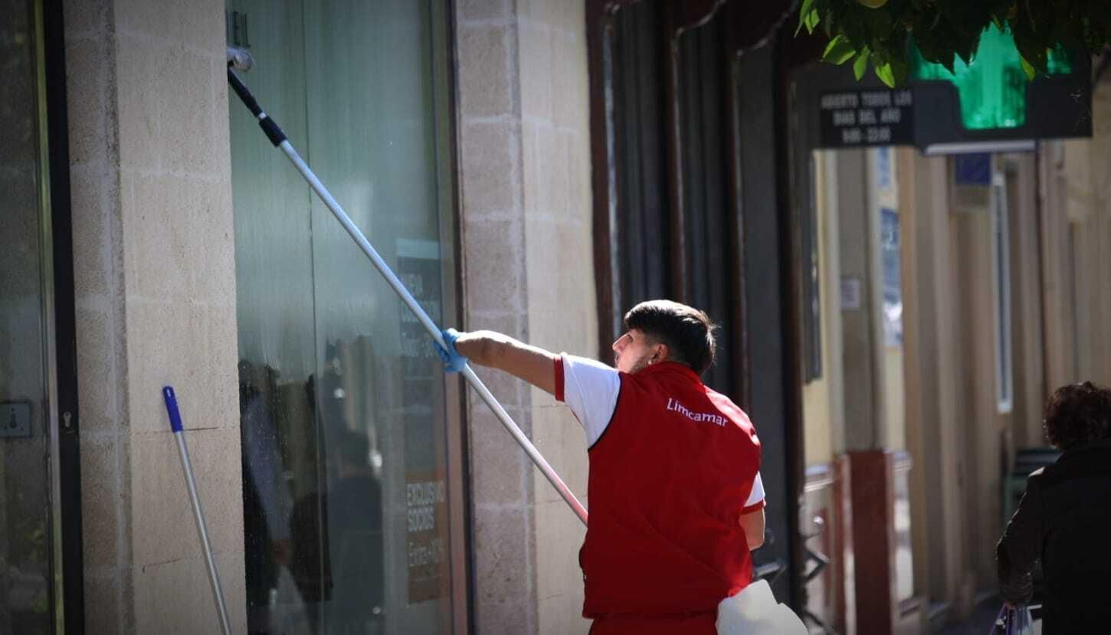 Un trabjador limpia los cristales del escaparate de una tienda del centro de Jerez.