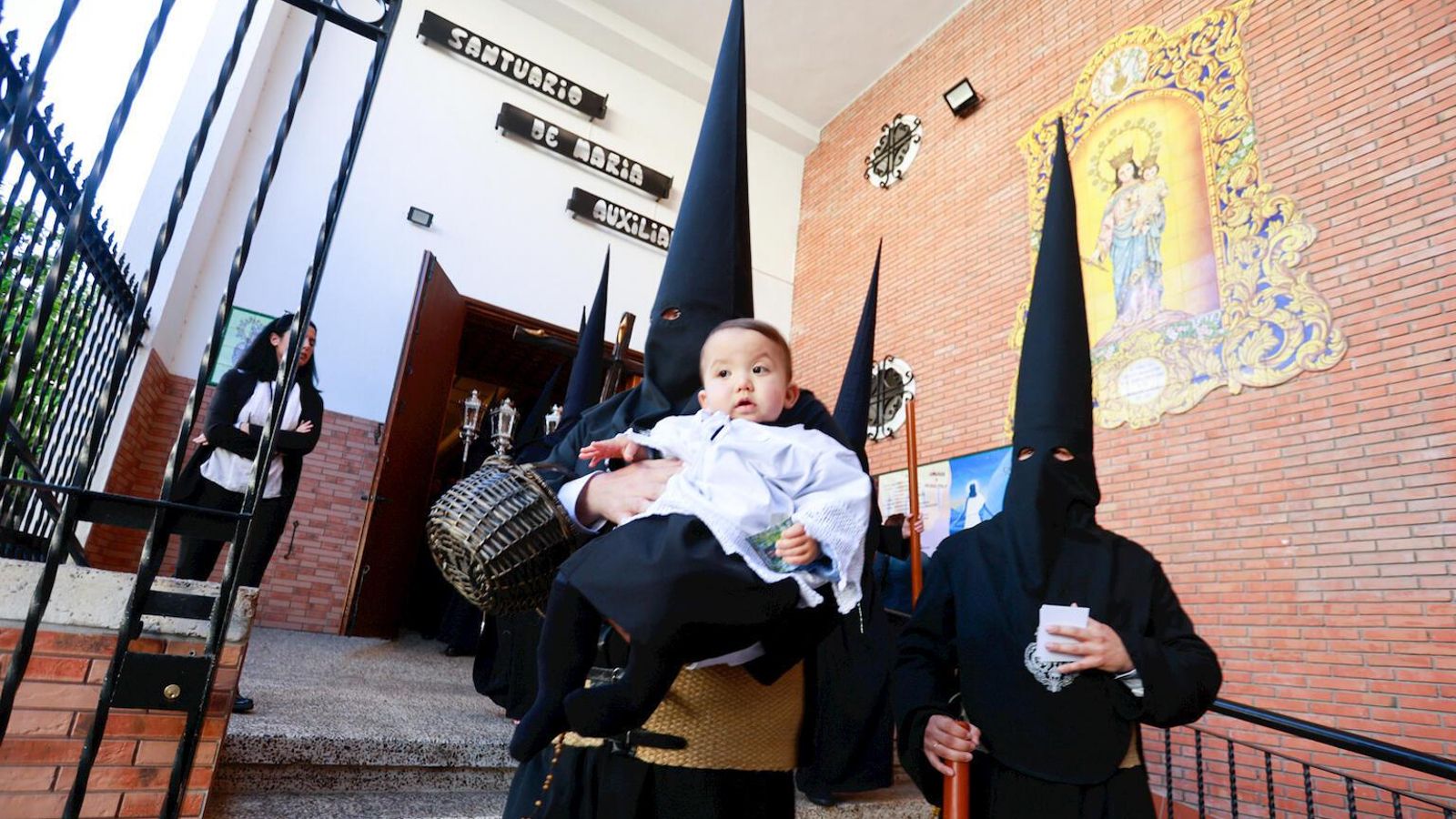 Un pequeño monaguillo en brazos de un penitente de la hermandad de Salesianos.