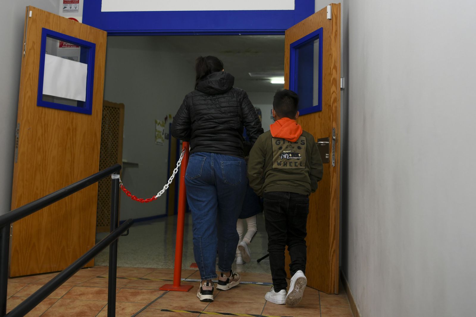 Dos niños abandonando una sala, acompañados por un adulto.
