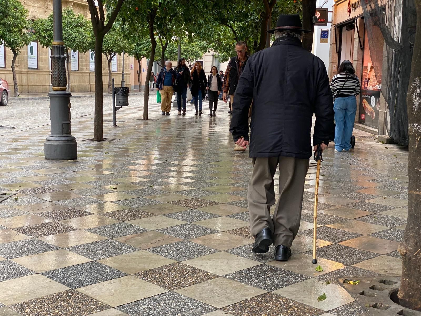 Una persona mayor pasea por la calle Larga con ayuda de un bastón.