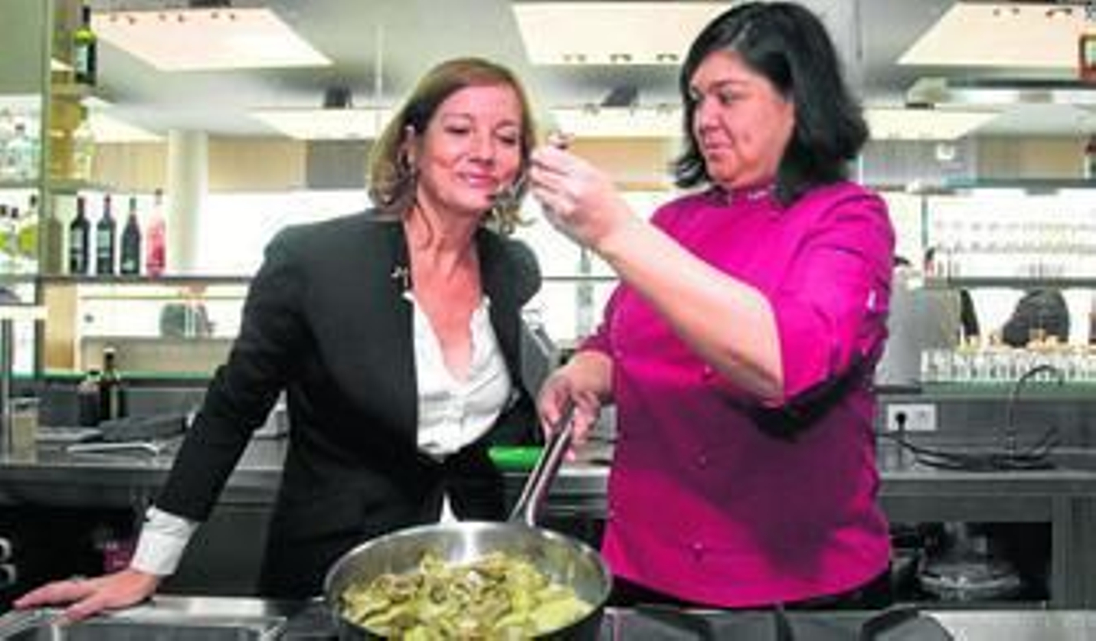 Celia jiménez da a probar a Anabel Carrillo unas alcachofas en salsa en la cocina de su nuevo restaurante, en el club deportivo Open Arena.