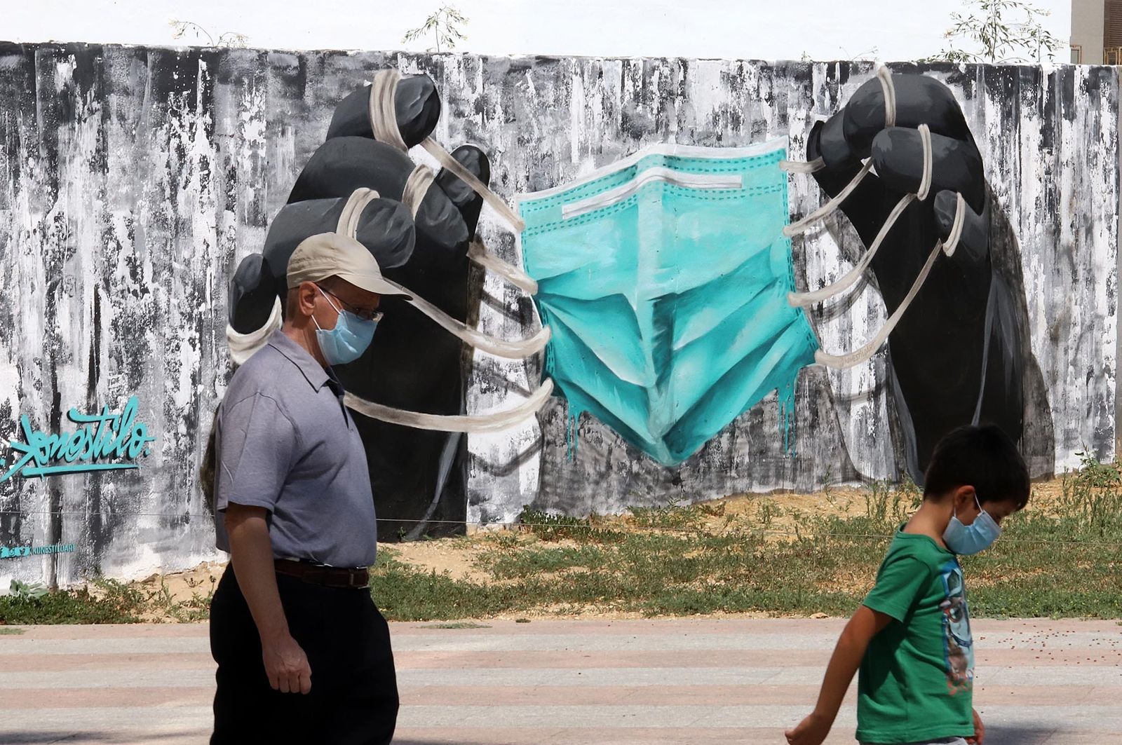 Un hombre y un niño con mascarillas pasan junto a un grafiti de una mascarilla