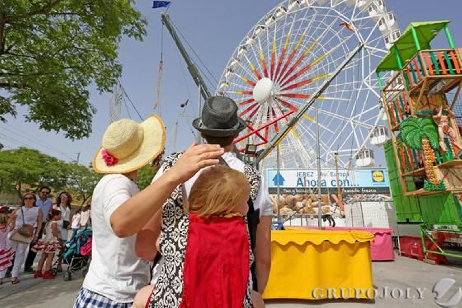 Una mujer protege a su hijo del calor con su mano mientras observa junto a su pareja la popular atracción de la noria. 

Foto: Pascual