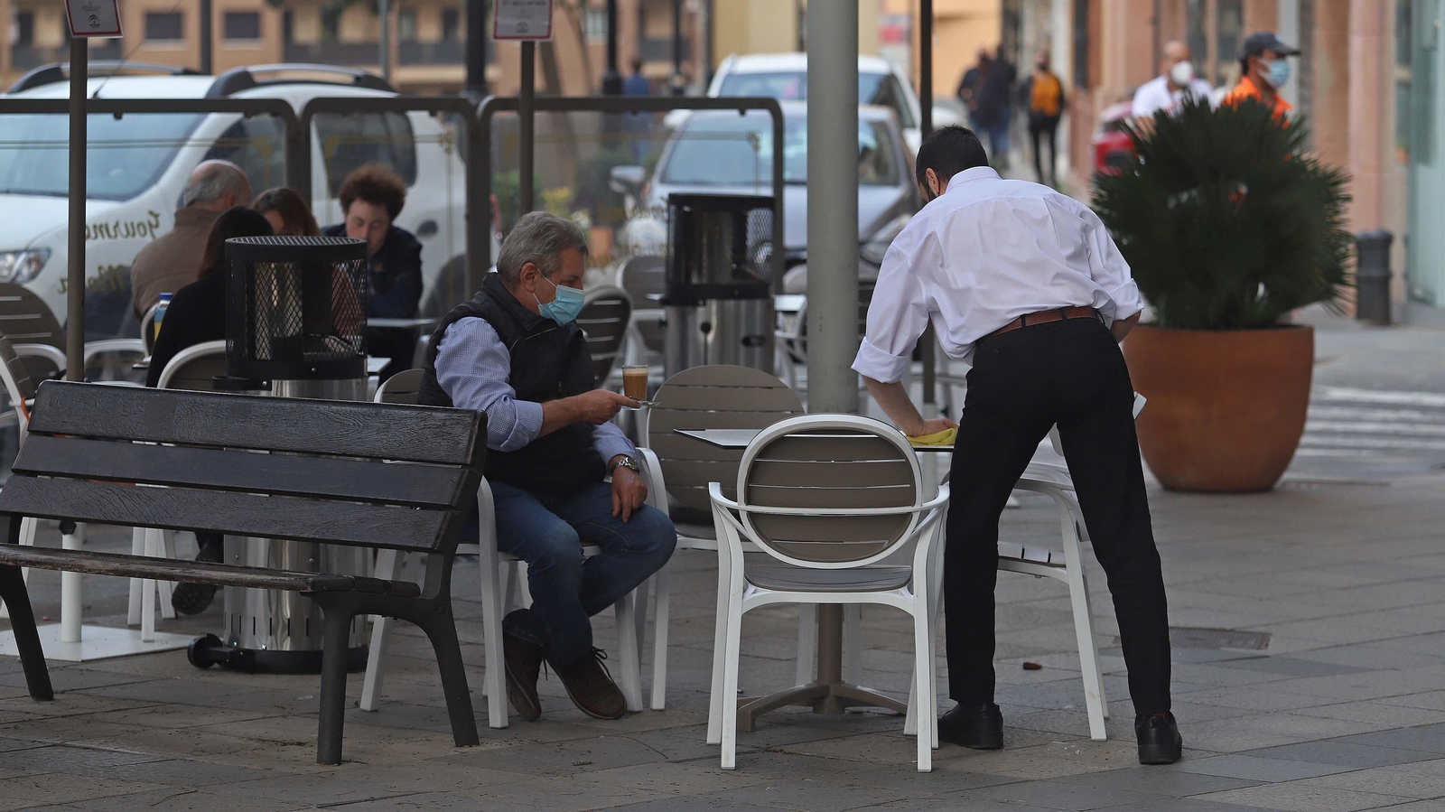 Un cliente sostiene un café mientras un camarero limpia la mesa.