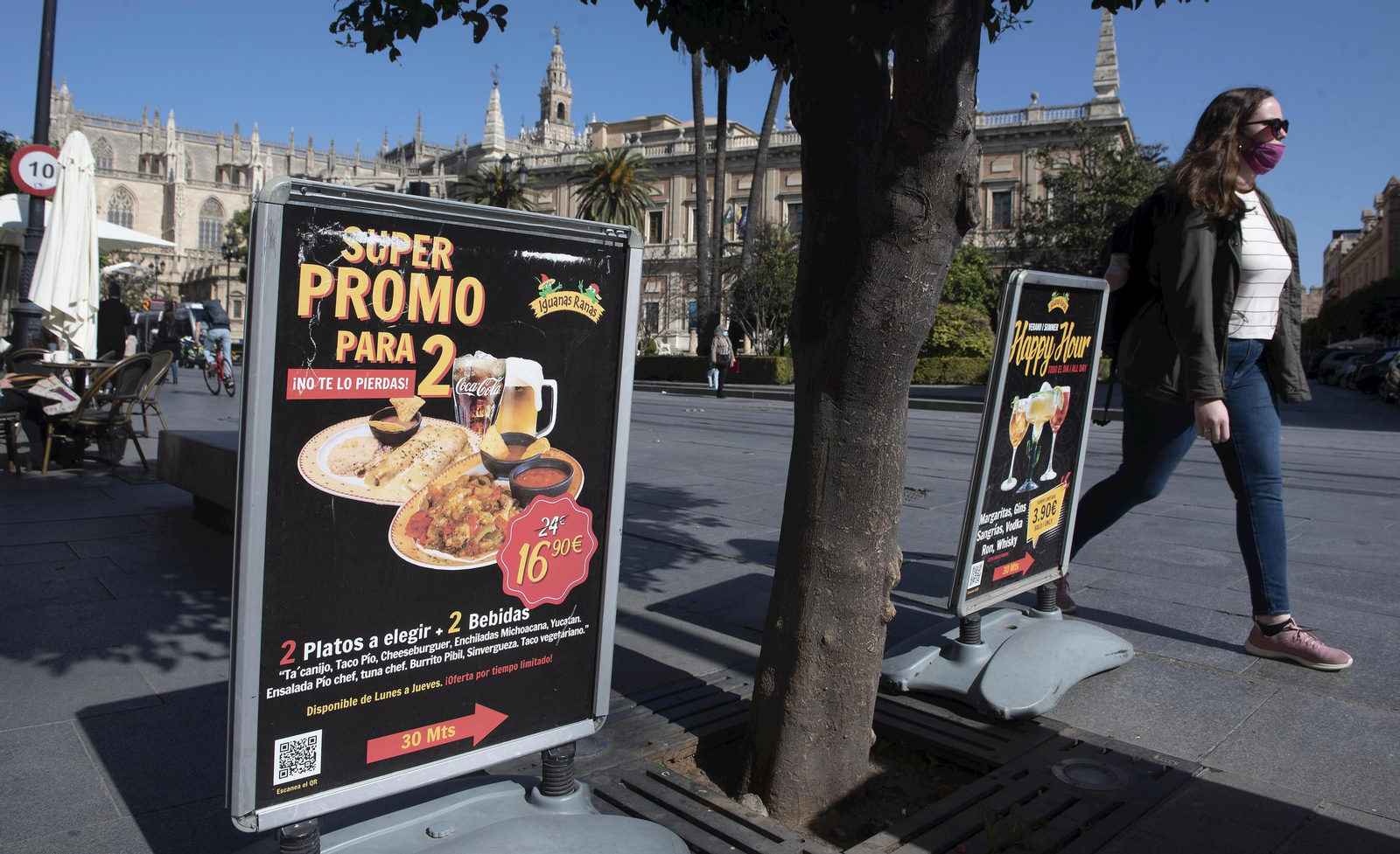 Una mujer camina junto a dos carteles de un negocio enclavado frente al Archivo de Indias.