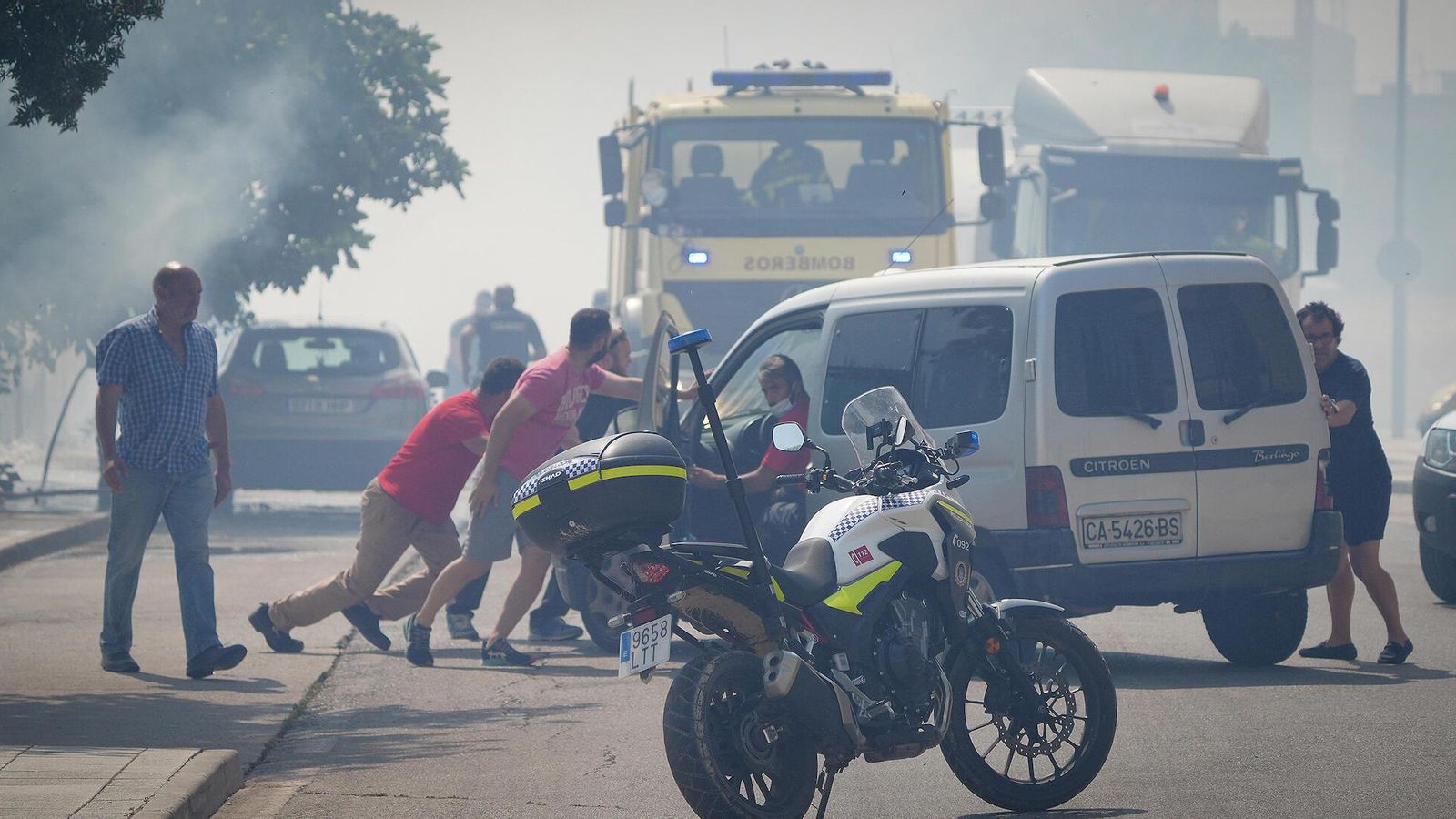 Vecinos ayudan a mover un vehículo expuesto a las llamas.