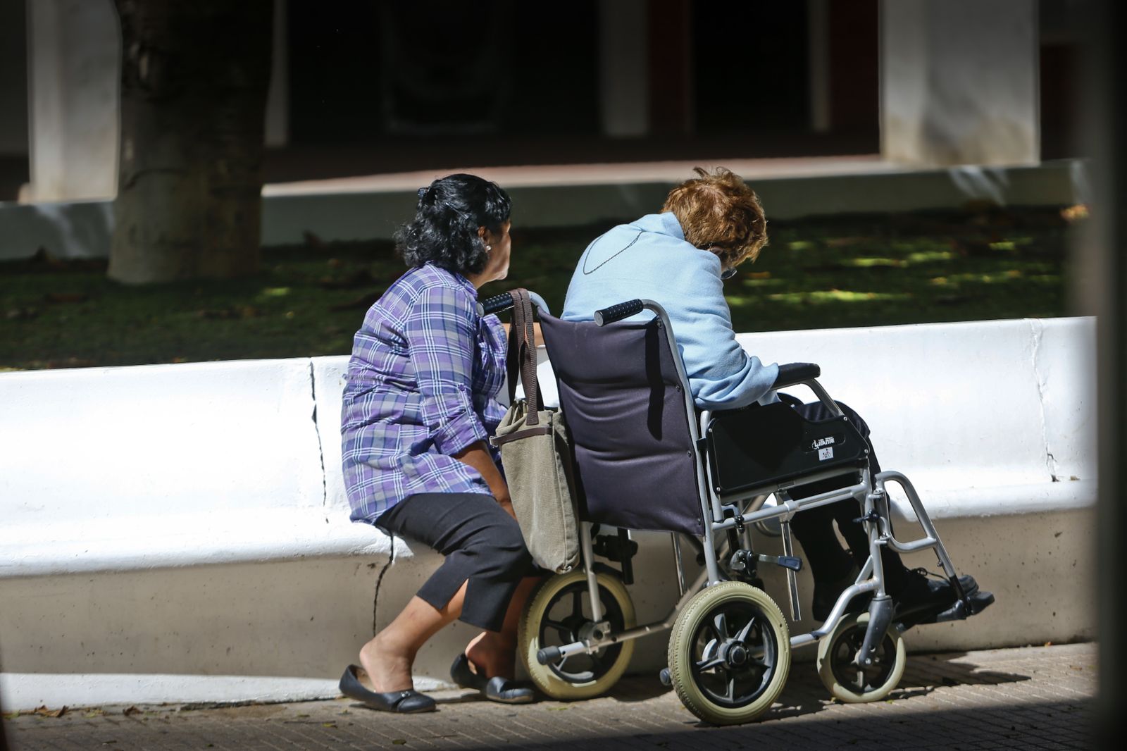 Una mujer descansa junto al carrito de una persona mayor con problemas de movilidad.