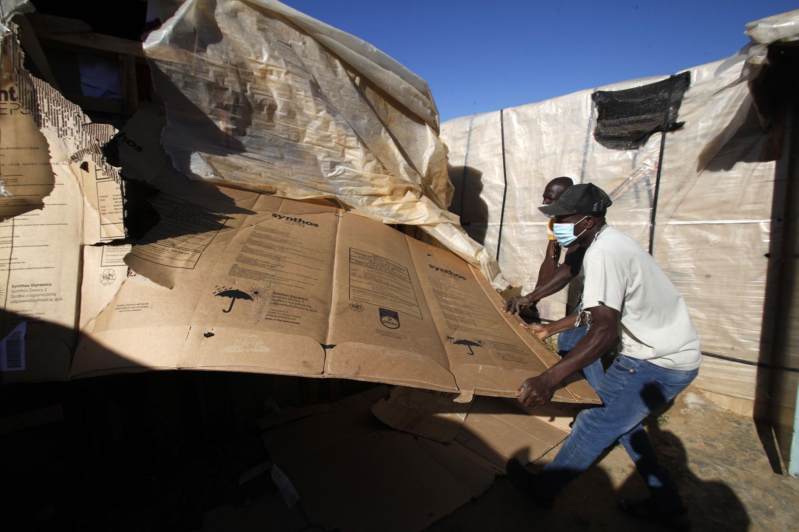 Dos de los beneficiarios desmantelan la chabola en la que vivían.