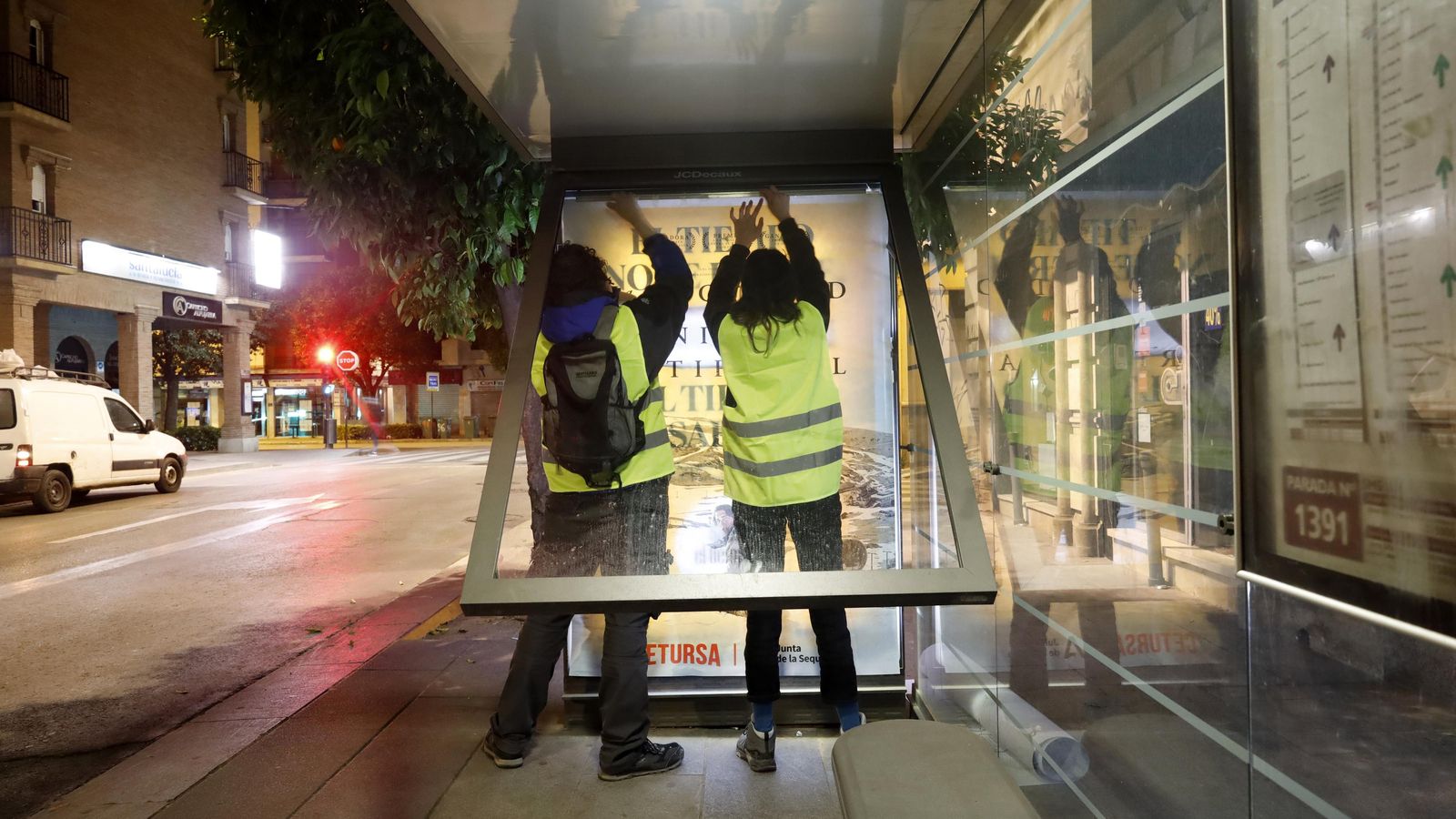 Dos operarios cambiando el cartél de una marquesina de autobúis