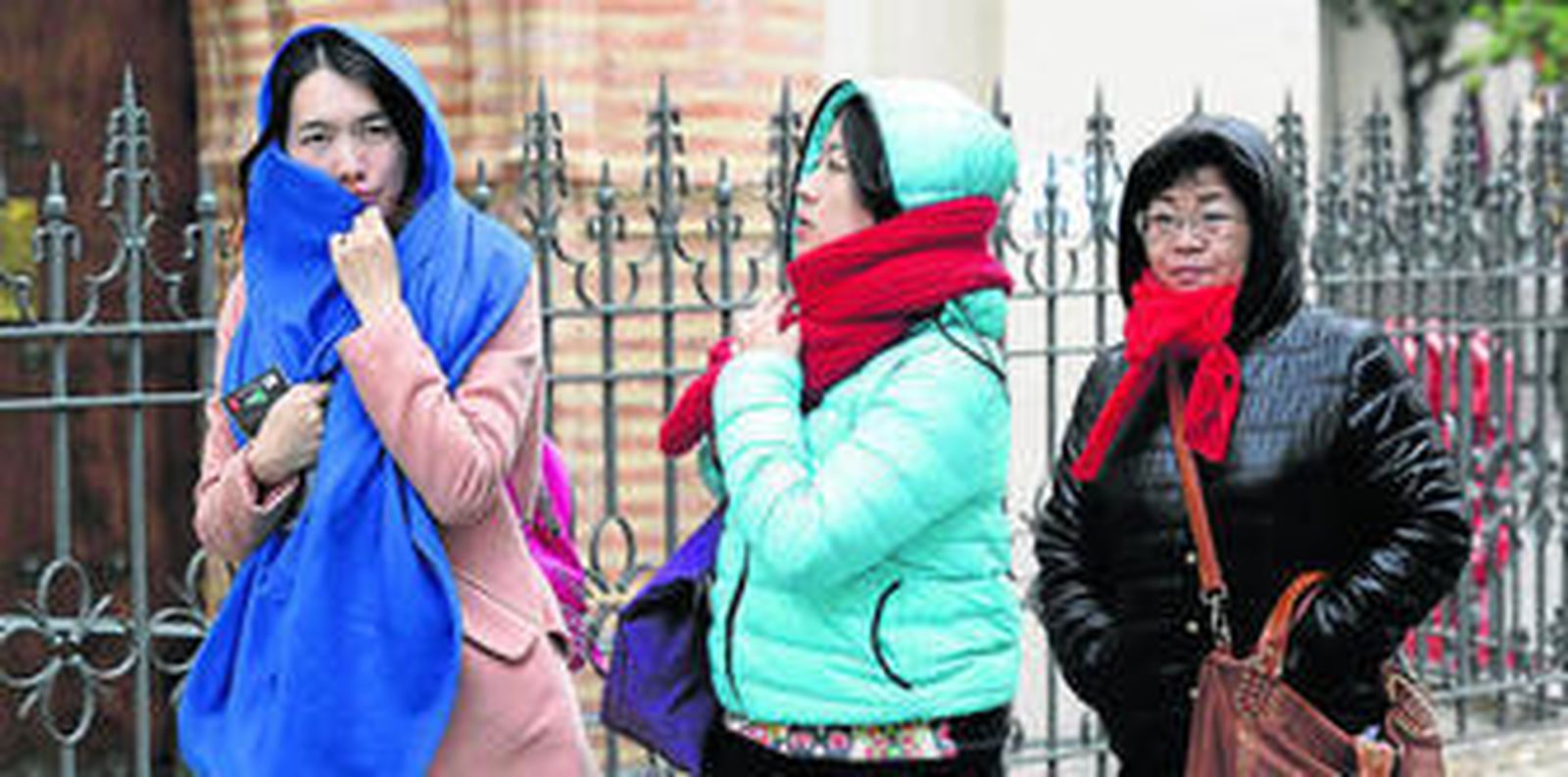 Tres turistas orientales se cubren de la tarde fría a su paso por Santa Catalina.