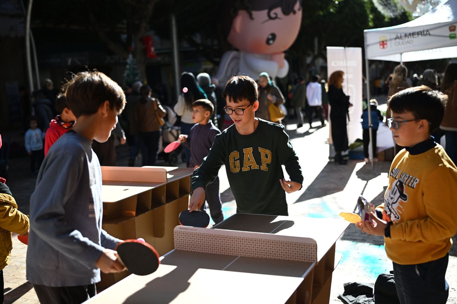 Grupos de niños juegan al ping pong en mini mesas de cartón.