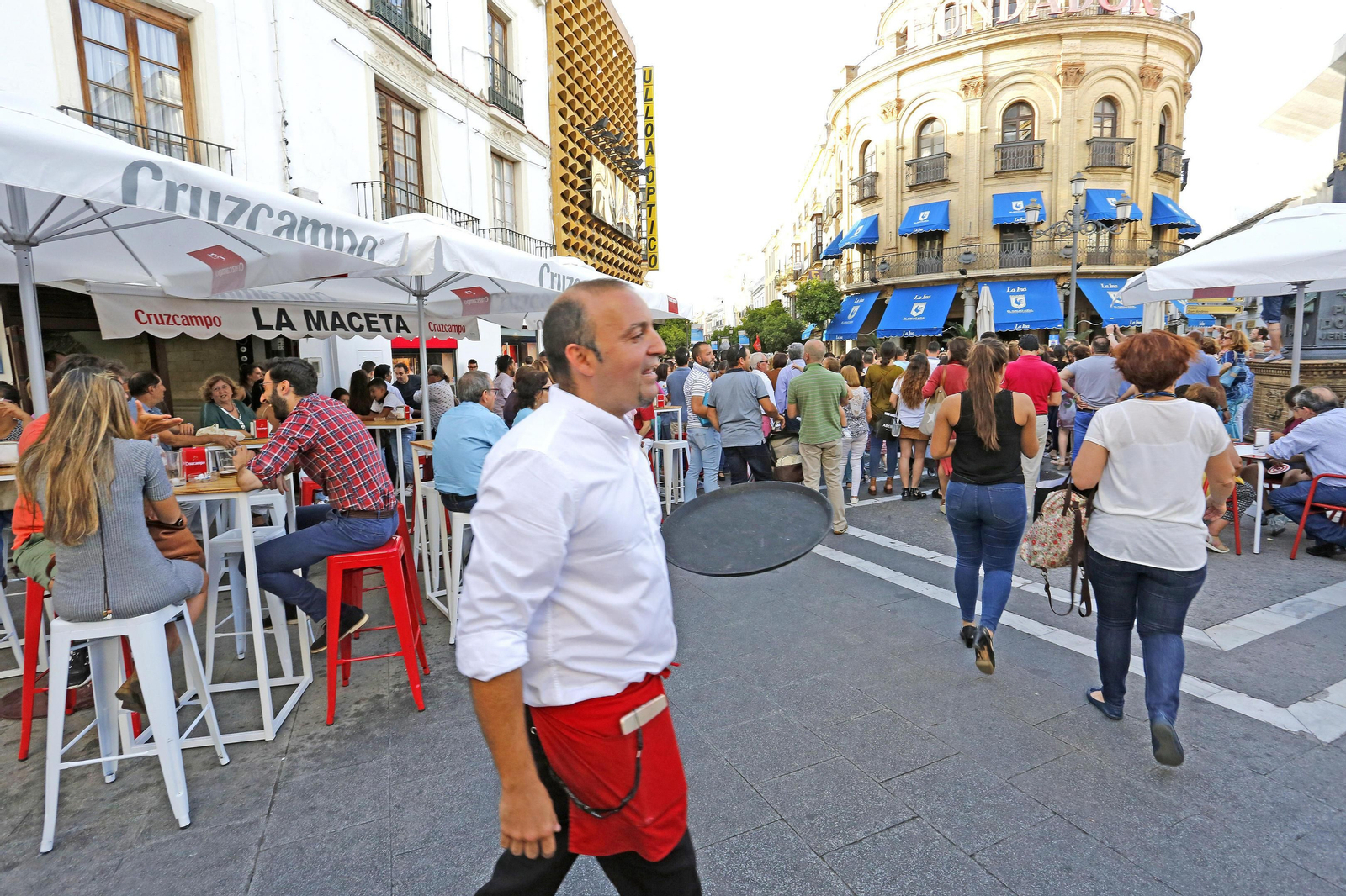 Un camarero en un céntrico bar con la terraza llena de clientes.