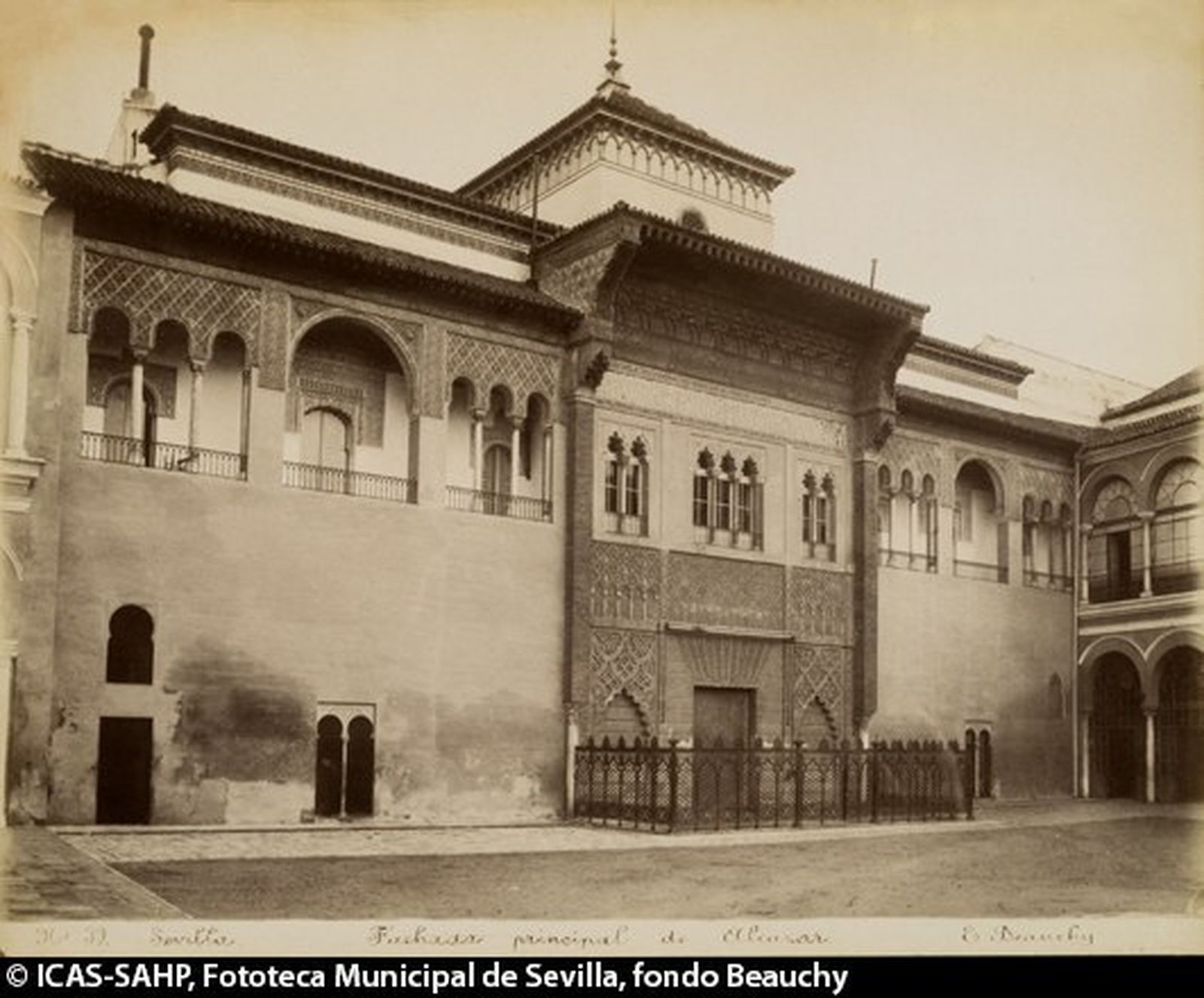 Vista general de la fachada del palacio del rey don Pedro I en el Patio de la Montería. La entrada, sobre la que hay instalado un toldo, está cerrada por una verja. A la derecha, la galería de acceso al salón del Almirante, cerrada con una reja.