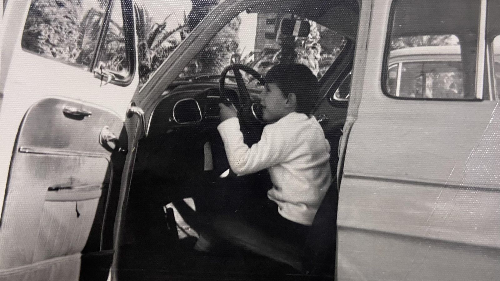 Un niño de los años 60, sentado en el asiento del piloto, hace como que conduce un Gordini