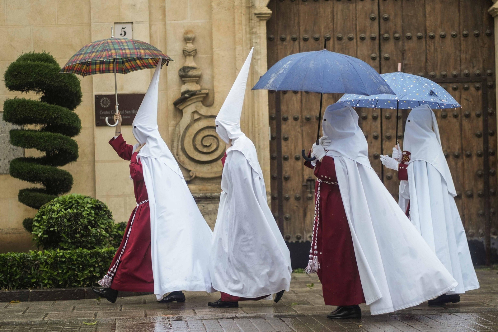 Unos penitentes tratan de refugiarse este Lunes Santo de la lluvia caída en Córdoba.