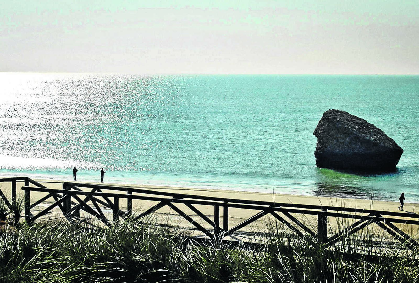 Preciosa imagen de un amanecer en la playa de Matalascañas, con dos turistas disfrutando del momento y un tercero corriendo por la arena.