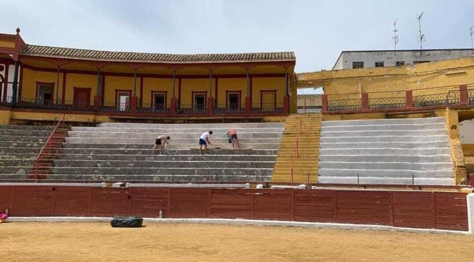 Alumnos de la escuela taurina limpiando y pintando las gradas de la plaza de toros de Écija.