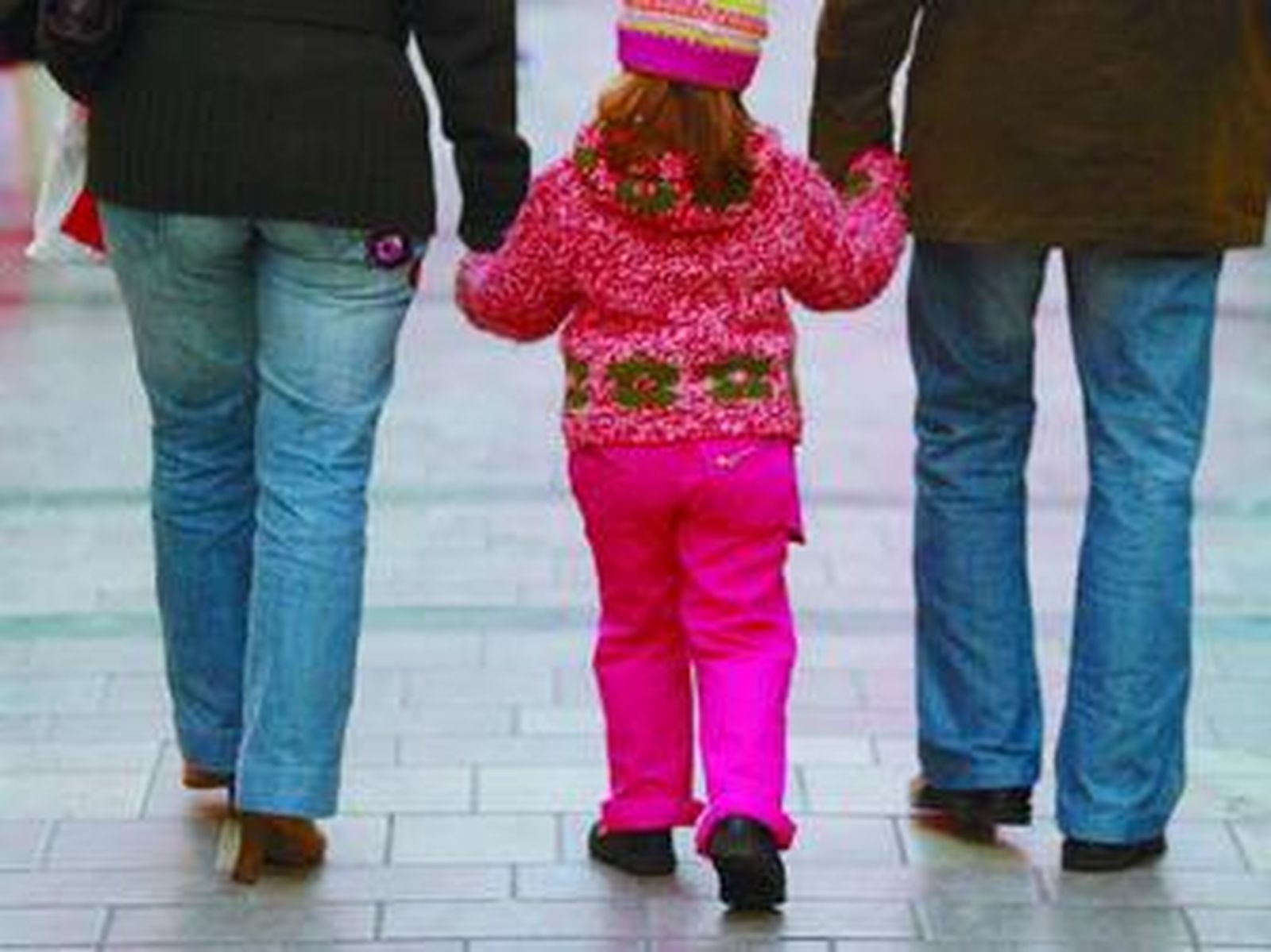 Una niña pasea de la mano de sus padres.
