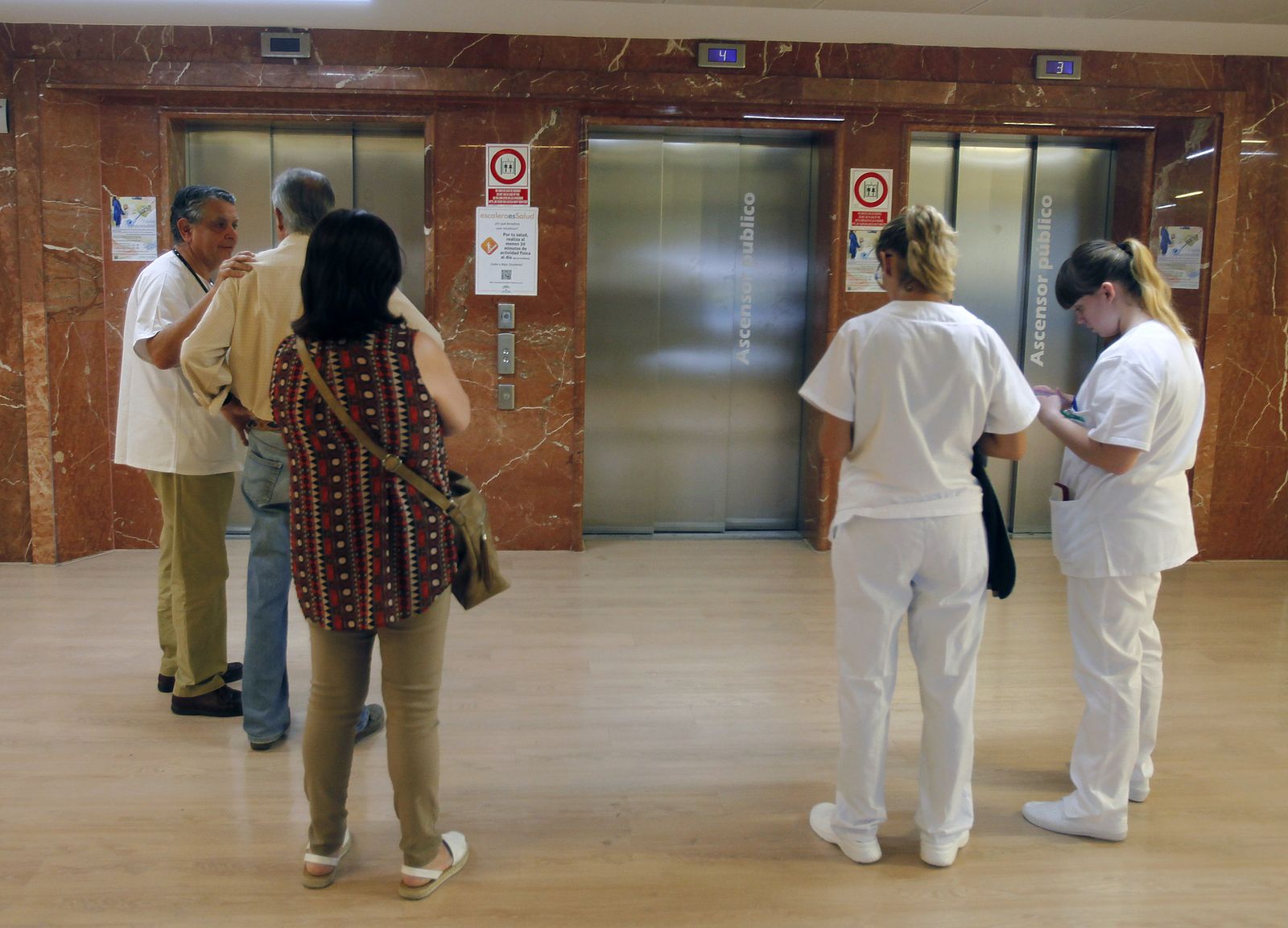 Usuarios y personal sanitario esperan en la zona de ascensores de un centro hospitalario.