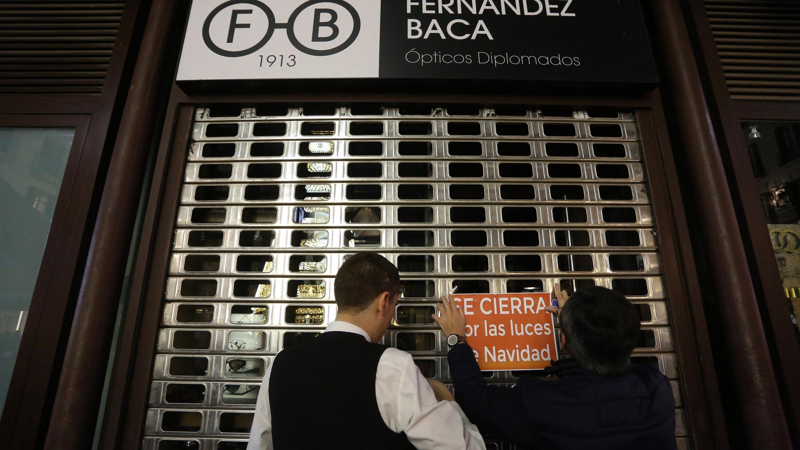 Un camarero ayuda a Manolo a colocar el cartel de cerrado en la joyería Fernández Baca.