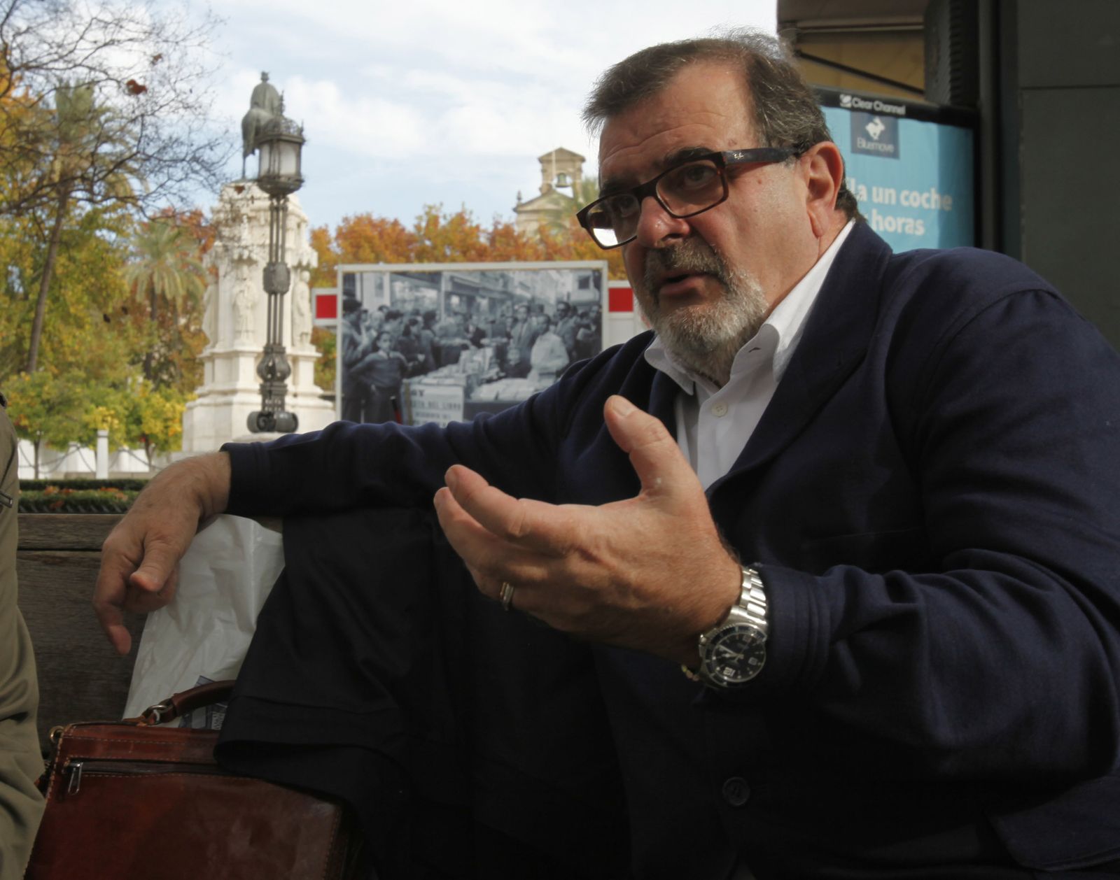 José Rodríguez de la Borbolla, en un banco de la Plaza Nueva, con San Fernando y el Ayuntamiento al fondo.
